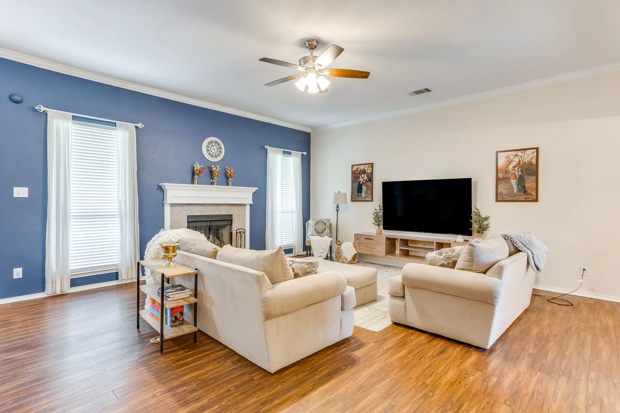 Living room featuring a traditional white-mantel and ceramic tile fireplace, and tall vertical windows with faux-wood blinds.