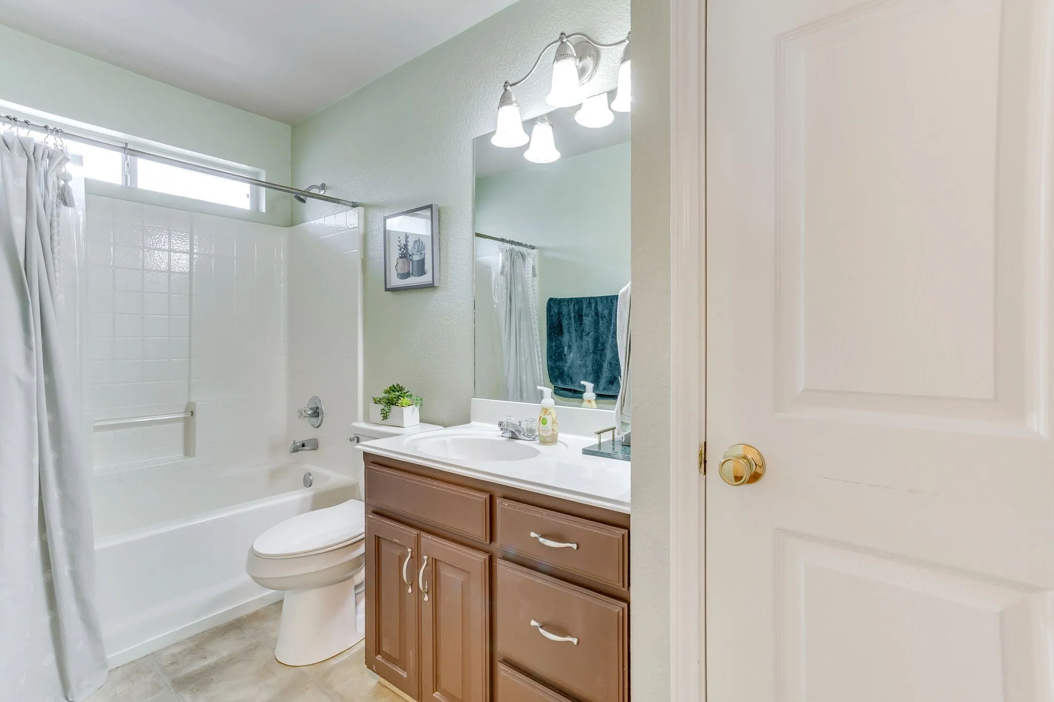 Bathroom featuring warm brown wood cabinets, solid white surface material, and a tub/shower combination with horizontal transom windows.