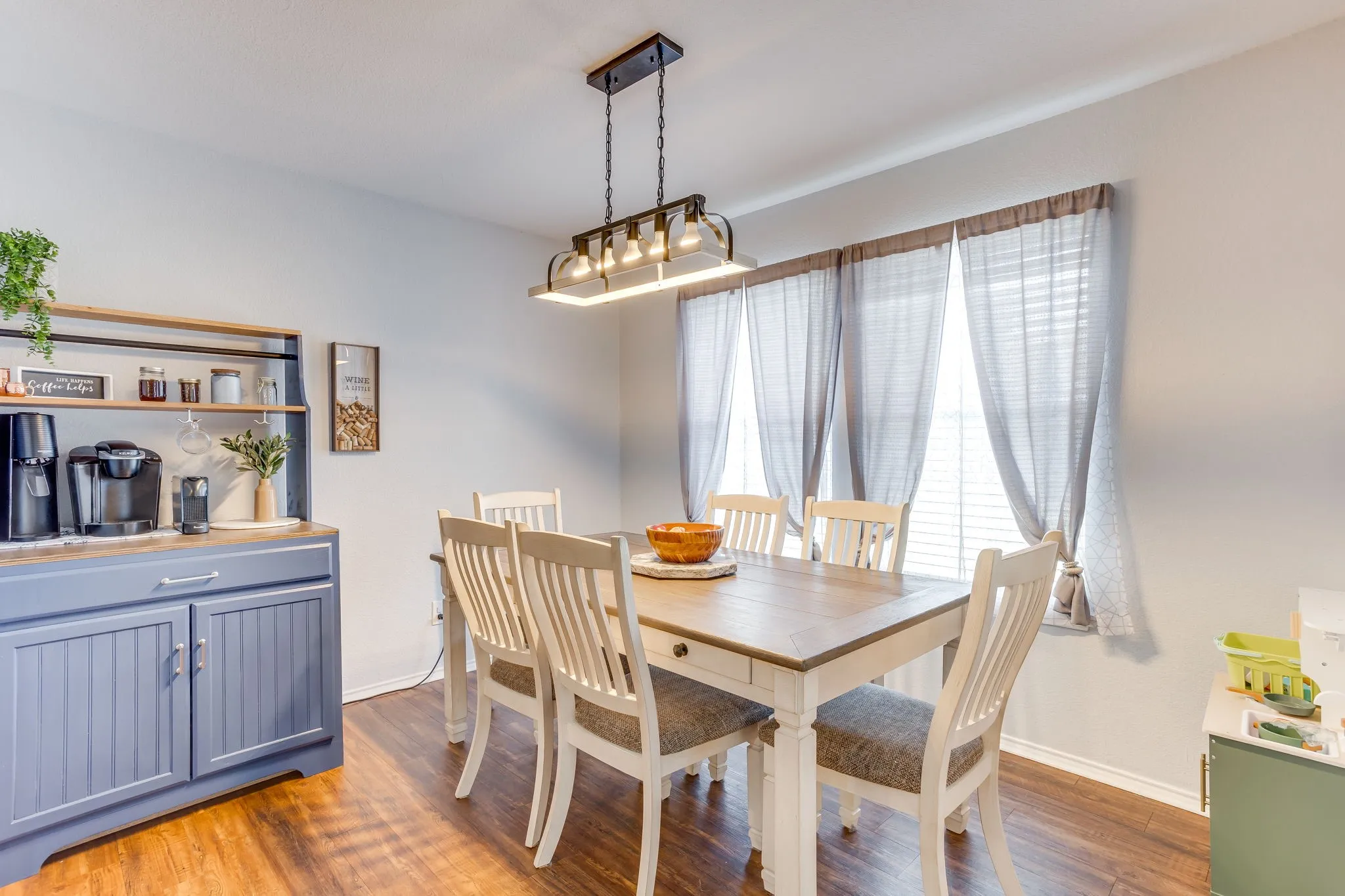 Dining area featuring neutral toned paint, medium-toned wood-style flooring, and multi-light linear fixture, and large vertical windows for abundant natural light.