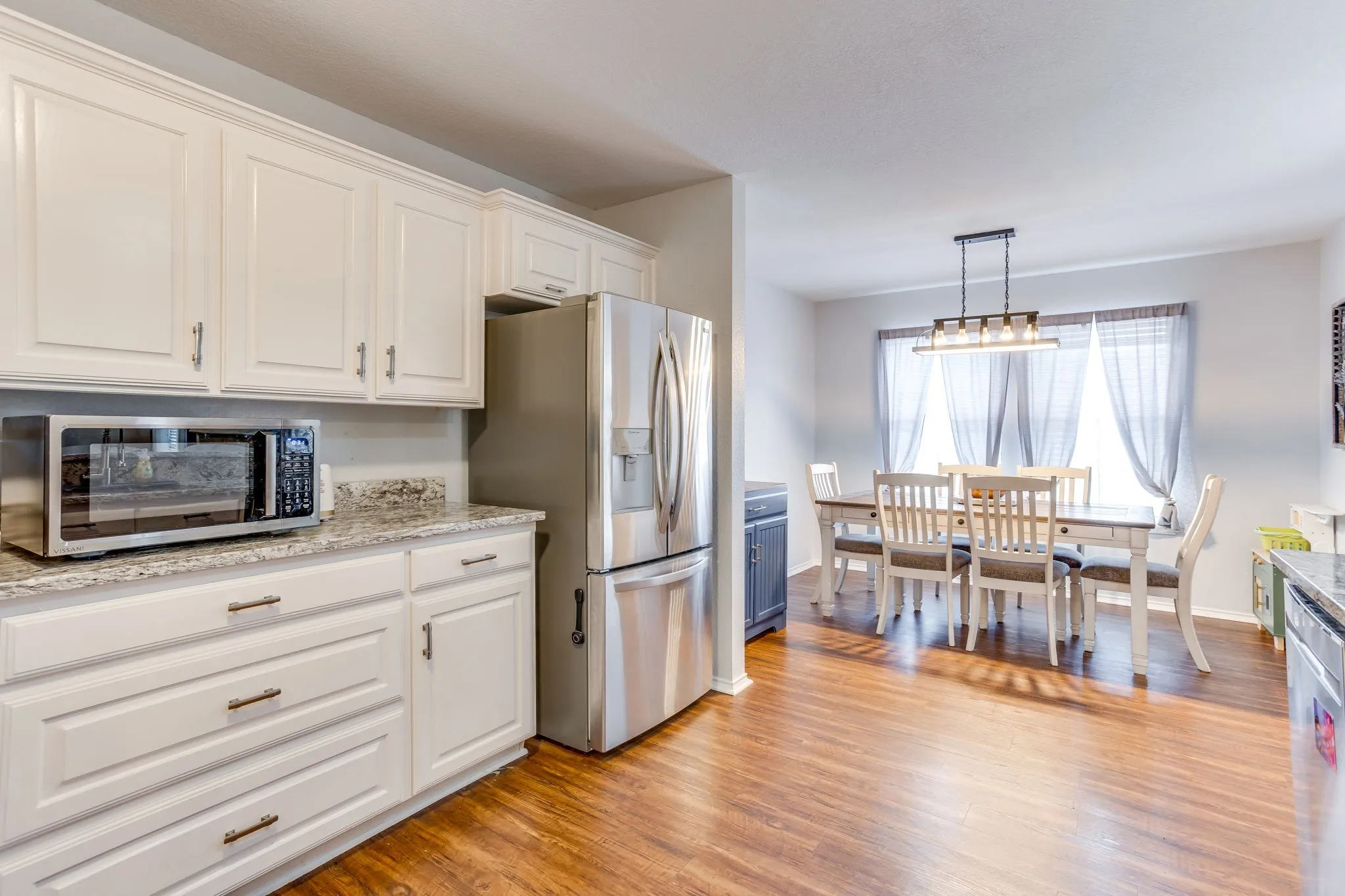 Kitchen featuring shaker-style cabinets painted in a clean white finish, polished granite featuring white, gray and black tones with a matching backsplash, and modern french door style stainless steel refrigerator.