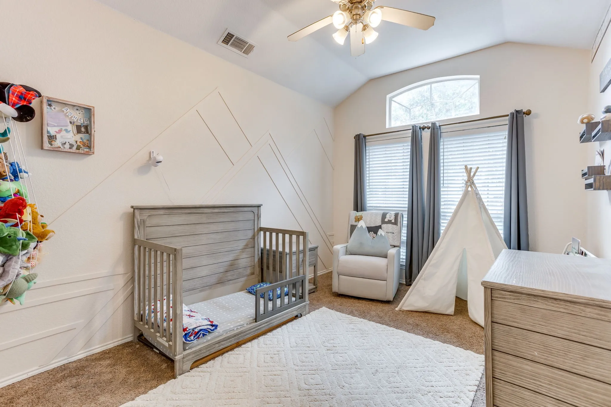 Bedroom featuring a cream/off-white painted wall featuring a modern, custom geometric design made of raised wooden accent slats, raised and angle ceiling, medium-to-dark brown carpeting.