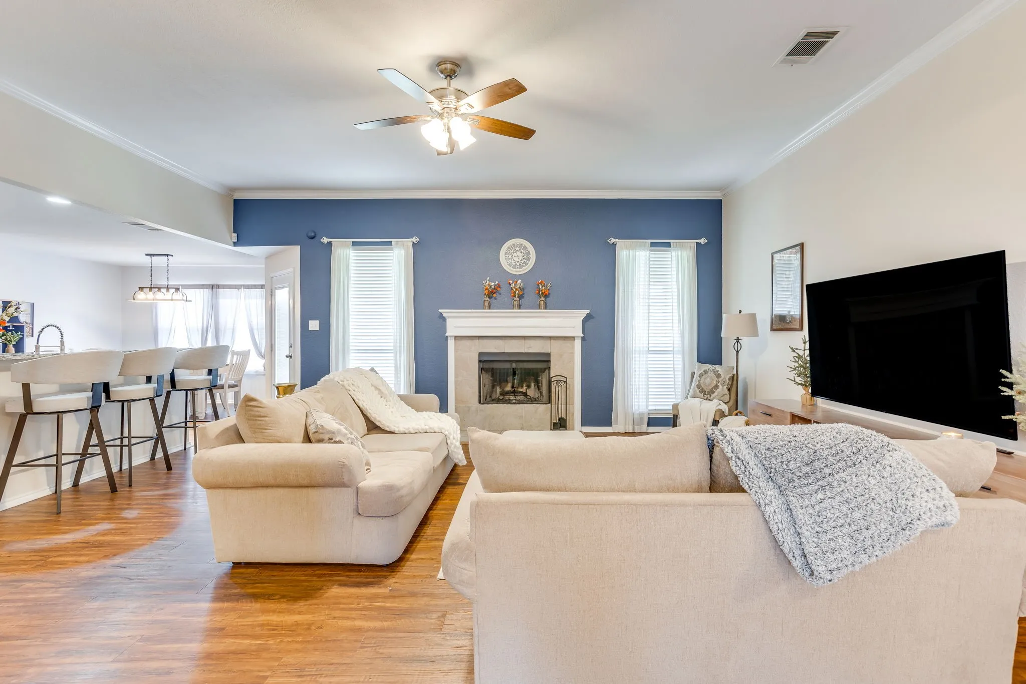 Living room featuring open-concept design that seamlessly connects the main living space to the kitchen and dining nook, with warm-toned wood-style flooring throughout.