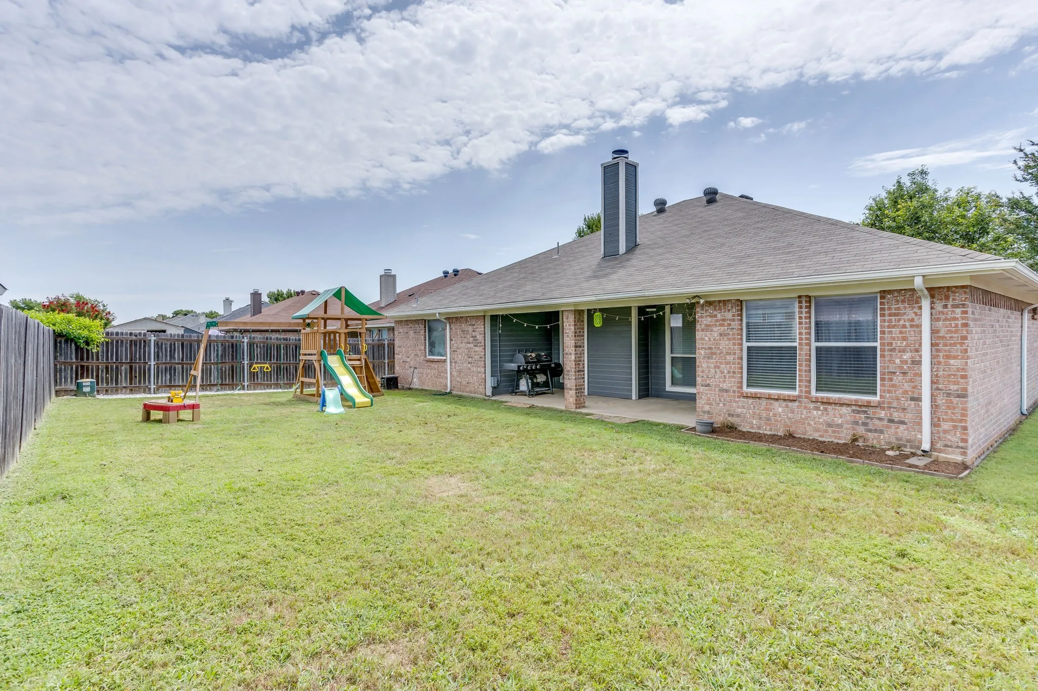Backyard featuring inset, covered concrete back porch providing shaded space, a yard boundary fully enclosed with a vertical wooden privacy fence.