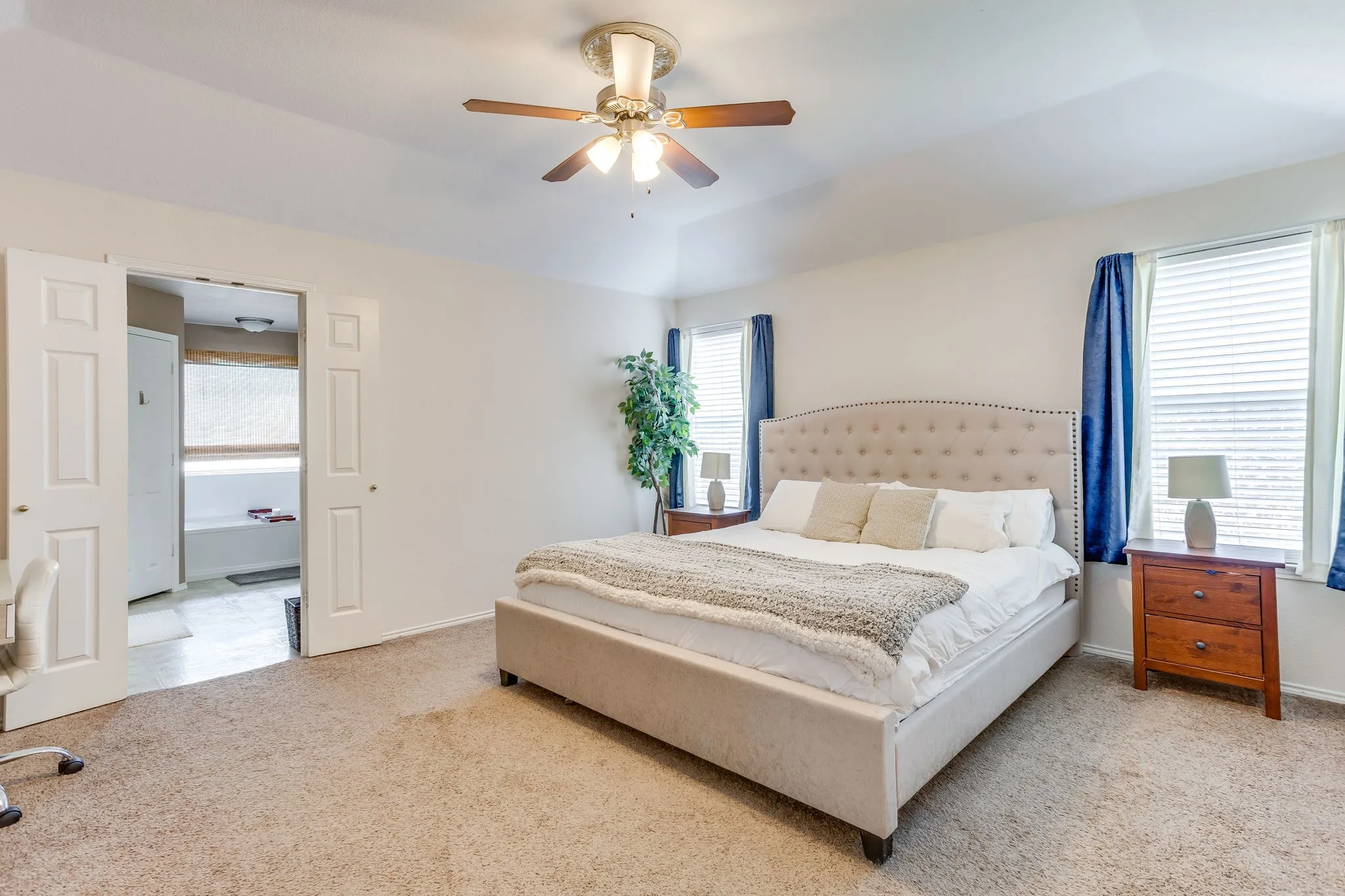 Primary bedroom featuring wall-to-wall carpeting in a neutral tone,  light neutral color painted walls, double doors finished in white, and two windows framing the room providing ample natural light.