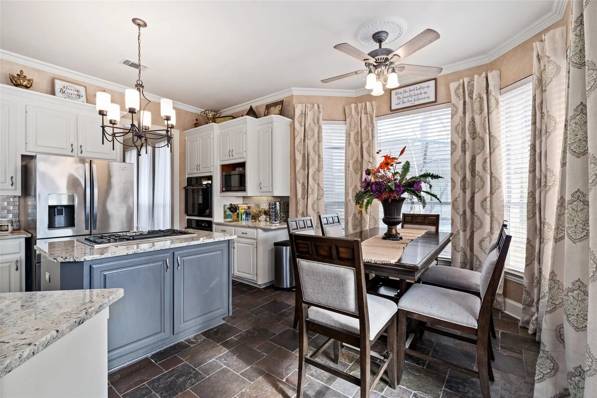 Kitchen featuring an island with a built-in cooktop, granite countertops, white cabinetry, and stainless steel appliances