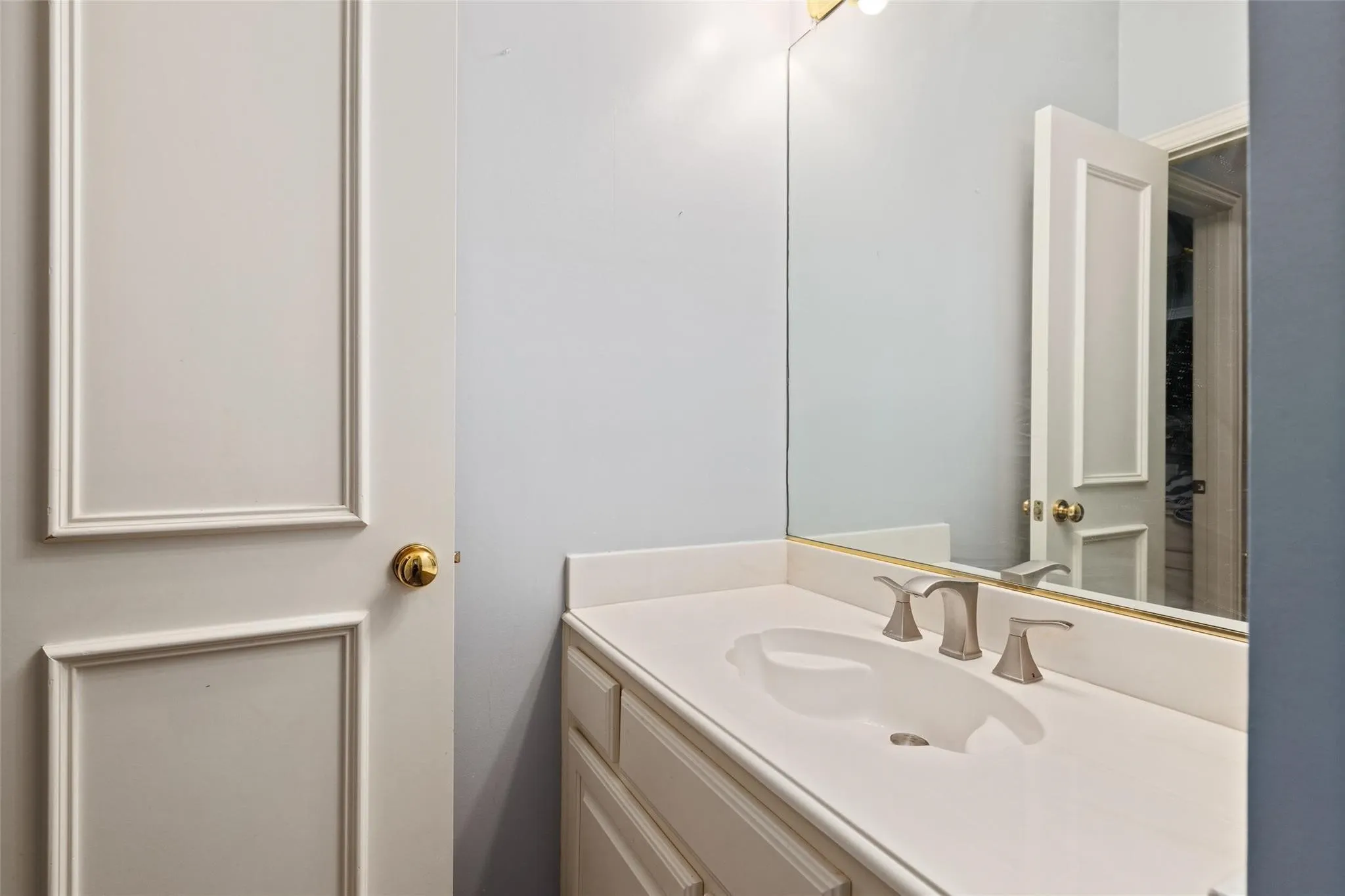 Vanity with an integrated sink, brushed nickel faucet, and a large mirror with a brass trim