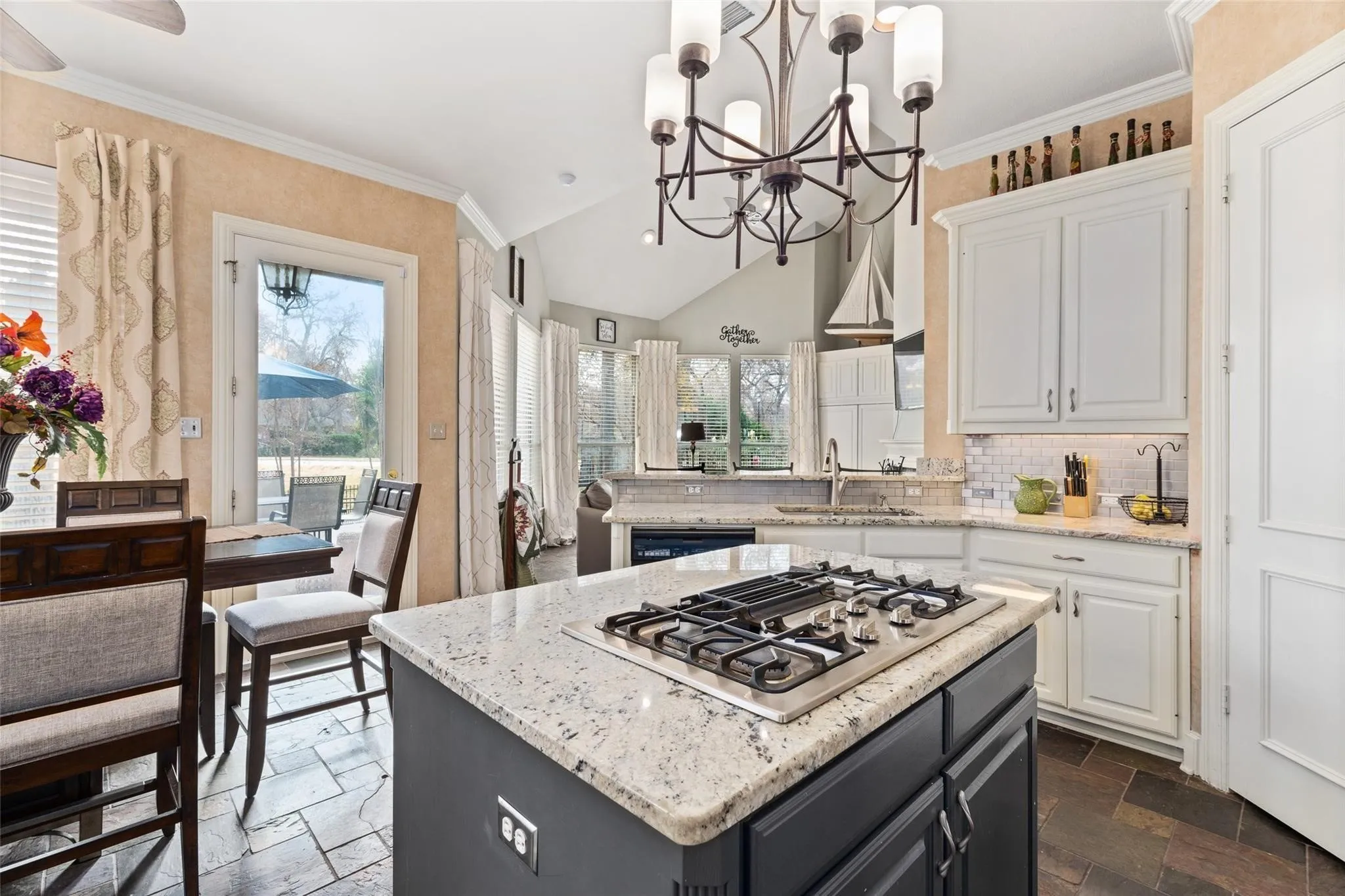 Gourmet kitchen featuring a central island with a gas cooktop, light-toned granite countertops, white cabinetry, a subway tile backsplash, and dark tile flooring