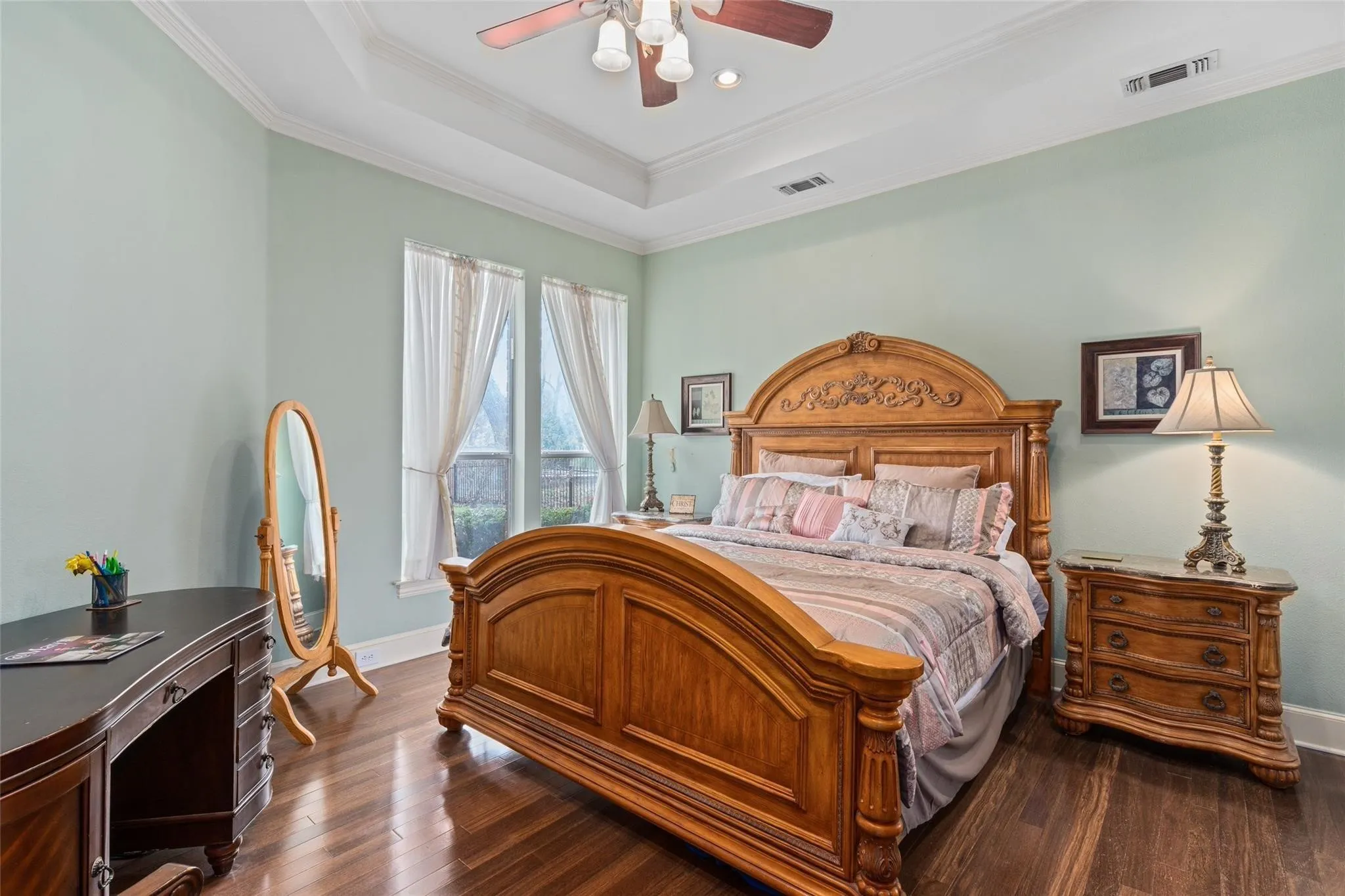 Spacious bedroom featuring wood-finish flooring, a tray ceiling, and two large windows