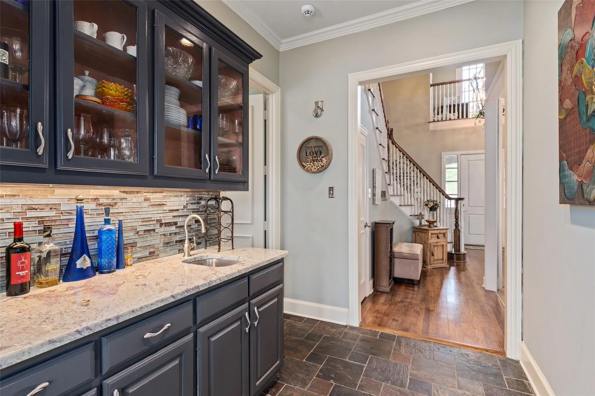 Wet bar featuring dark cabinetry, glass-front upper cabinets with interior lighting, a mosaic tile backsplash, and a built-in sink with a gooseneck faucet