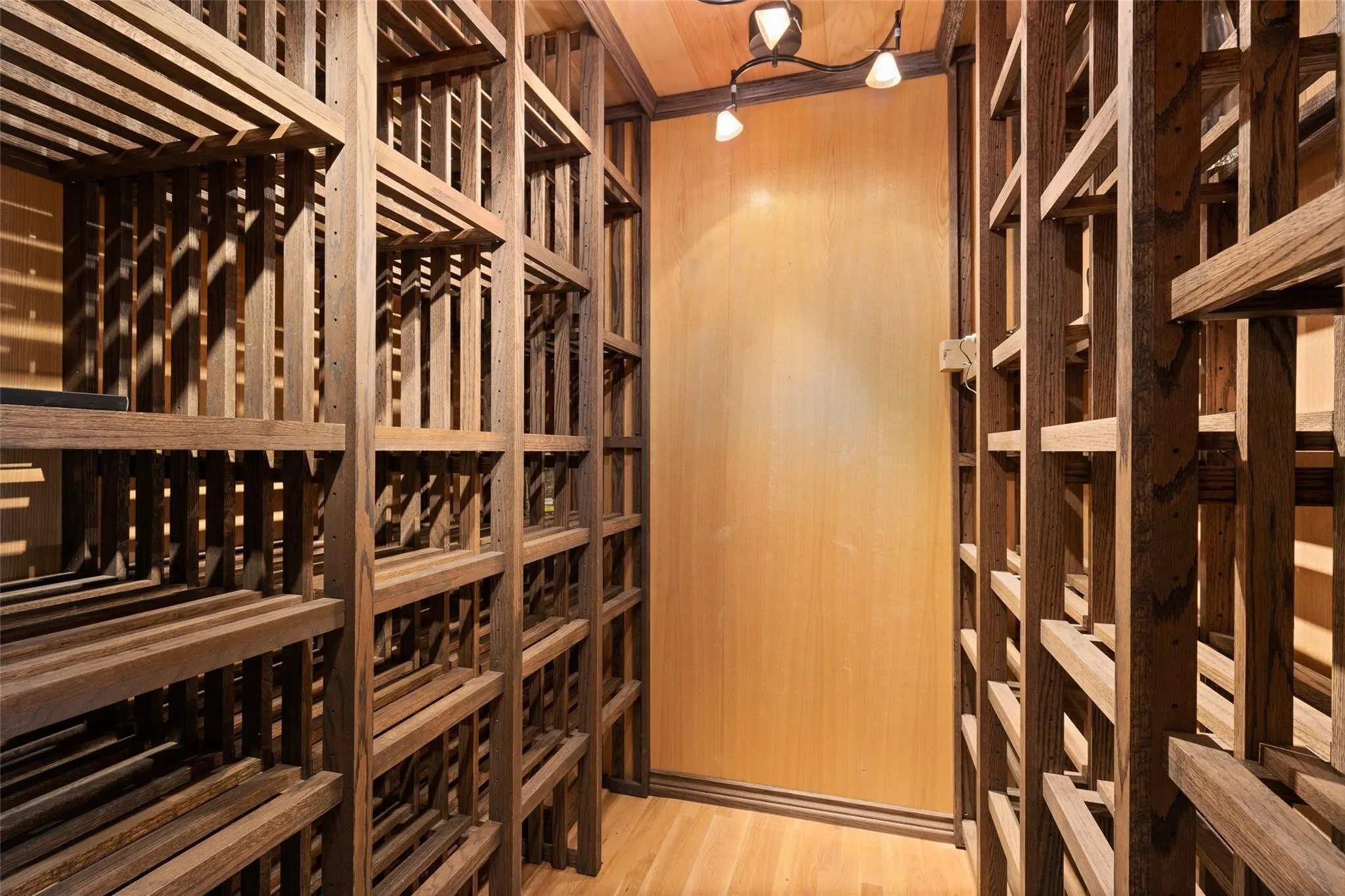 Custom wood wine storage featuring slatted shelving, wood-finish flooring, and recessed track lighting