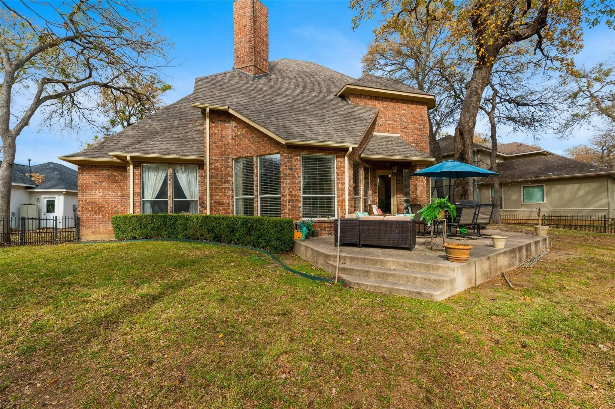 Brick exterior with a prominent chimney, a multi-level concrete patio, and a manicured hedge