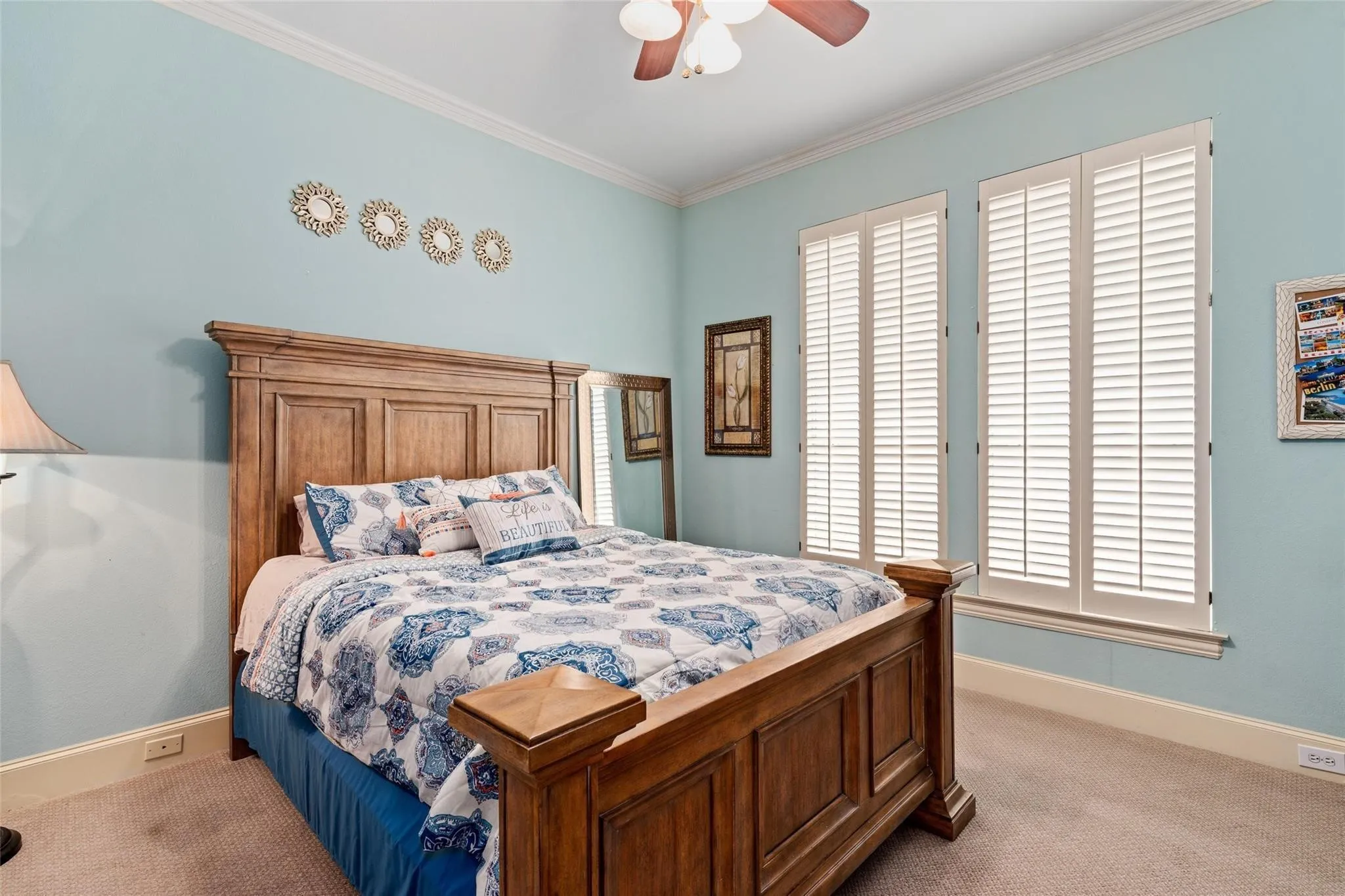 Spacious room featuring dual windows with interior shutters, crown molding, a ceiling fan, and wall-to-wall carpeting