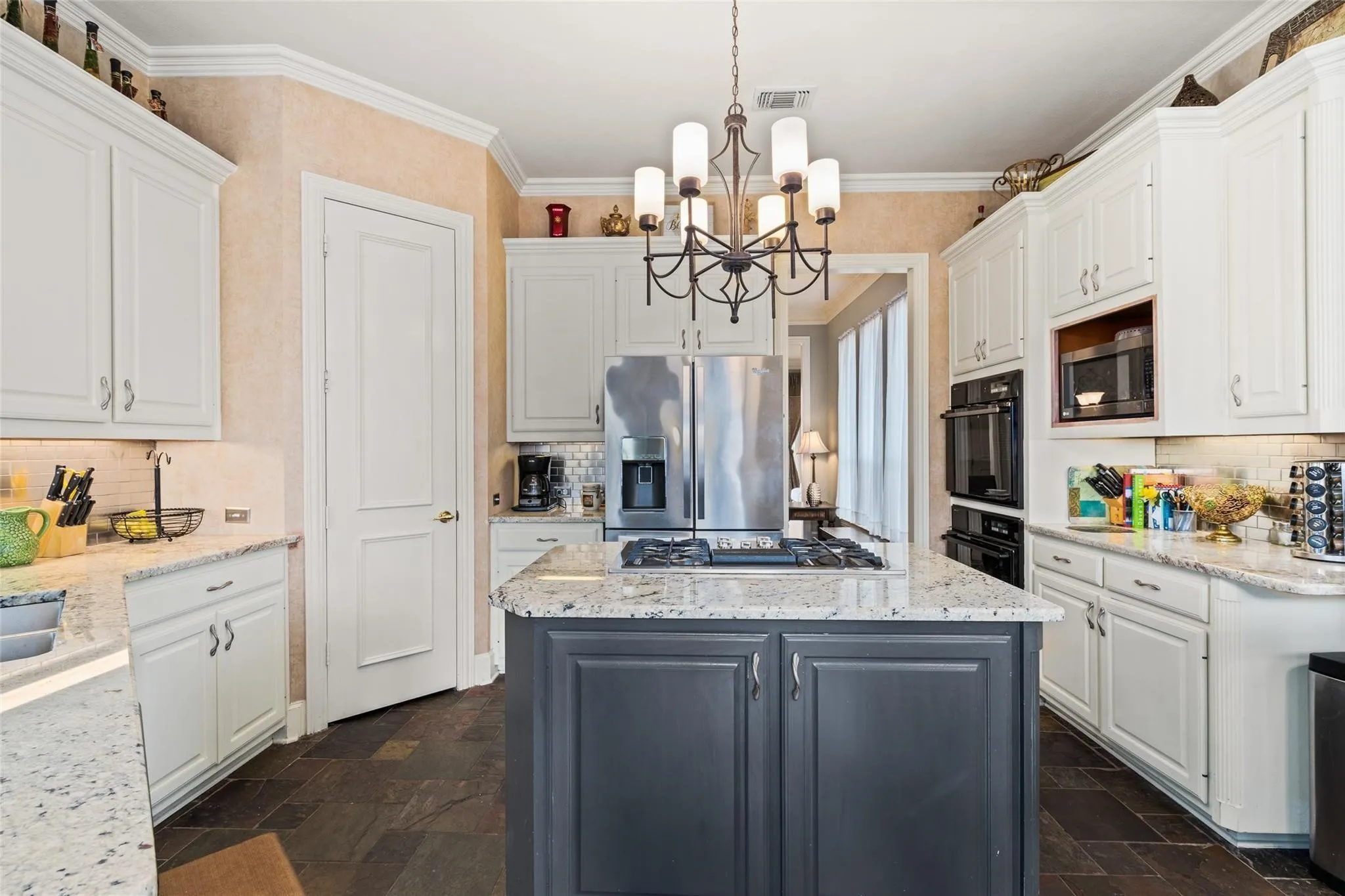 Gourmet kitchen featuring a dark grey island with a gas cooktop, white perimeter cabinetry, light speckled countertops, and dark slate tile flooring