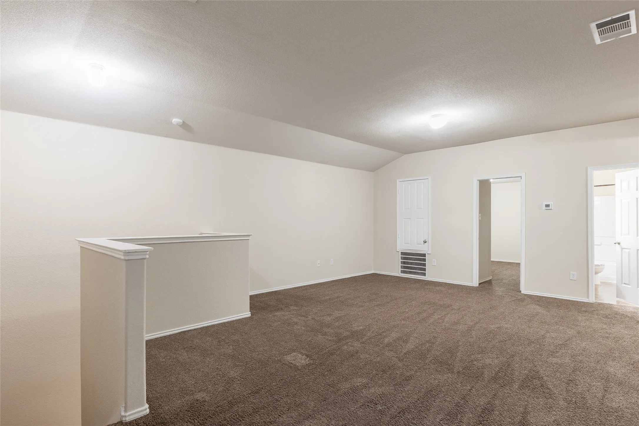 Spacious room featuring vaulted ceilings, light-colored walls, and neutral carpet flooring