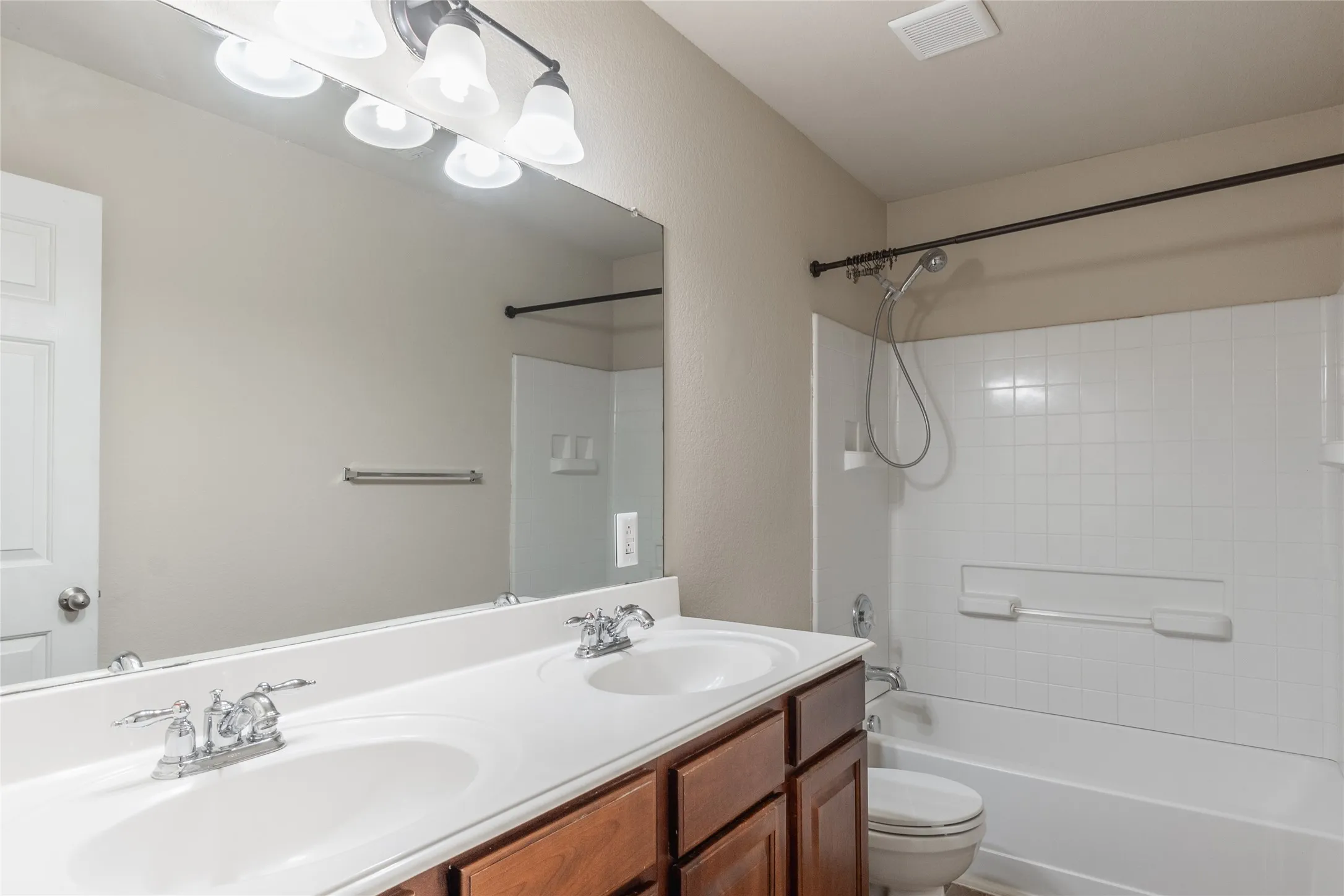 Bathroom featuring a dual-sink vanity with a white countertop, wood-finish cabinetry, and chrome fixtures