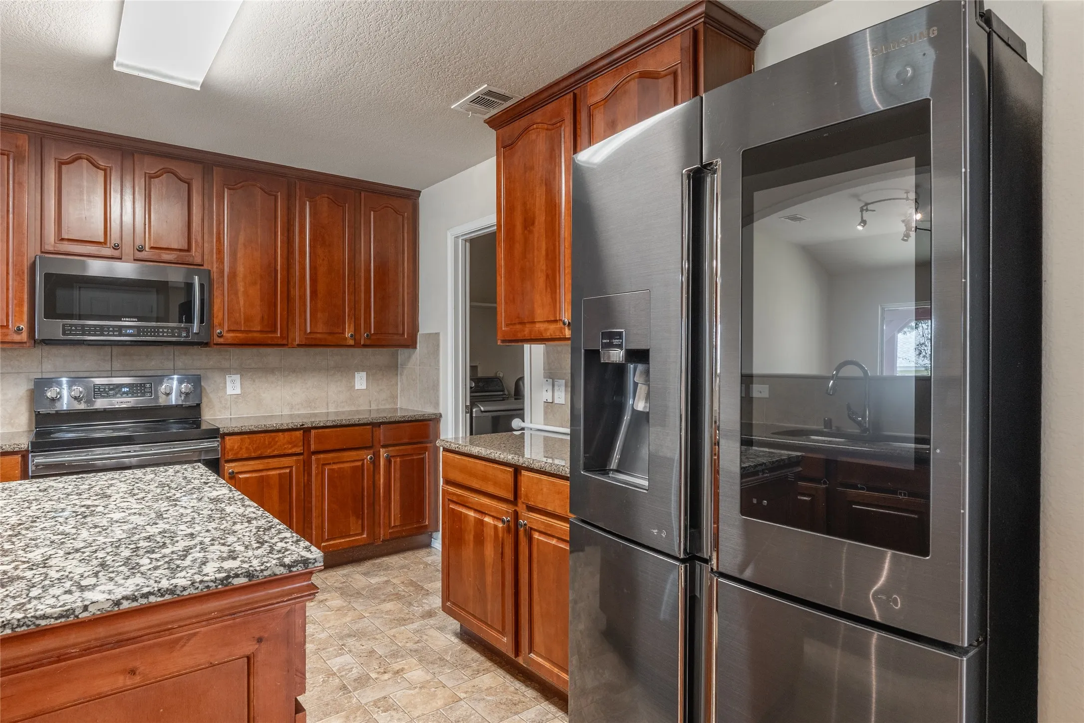 Kitchen featuring wood-finish cabinetry, stainless steel appliances, granite countertops, tile backsplash, and tile flooring