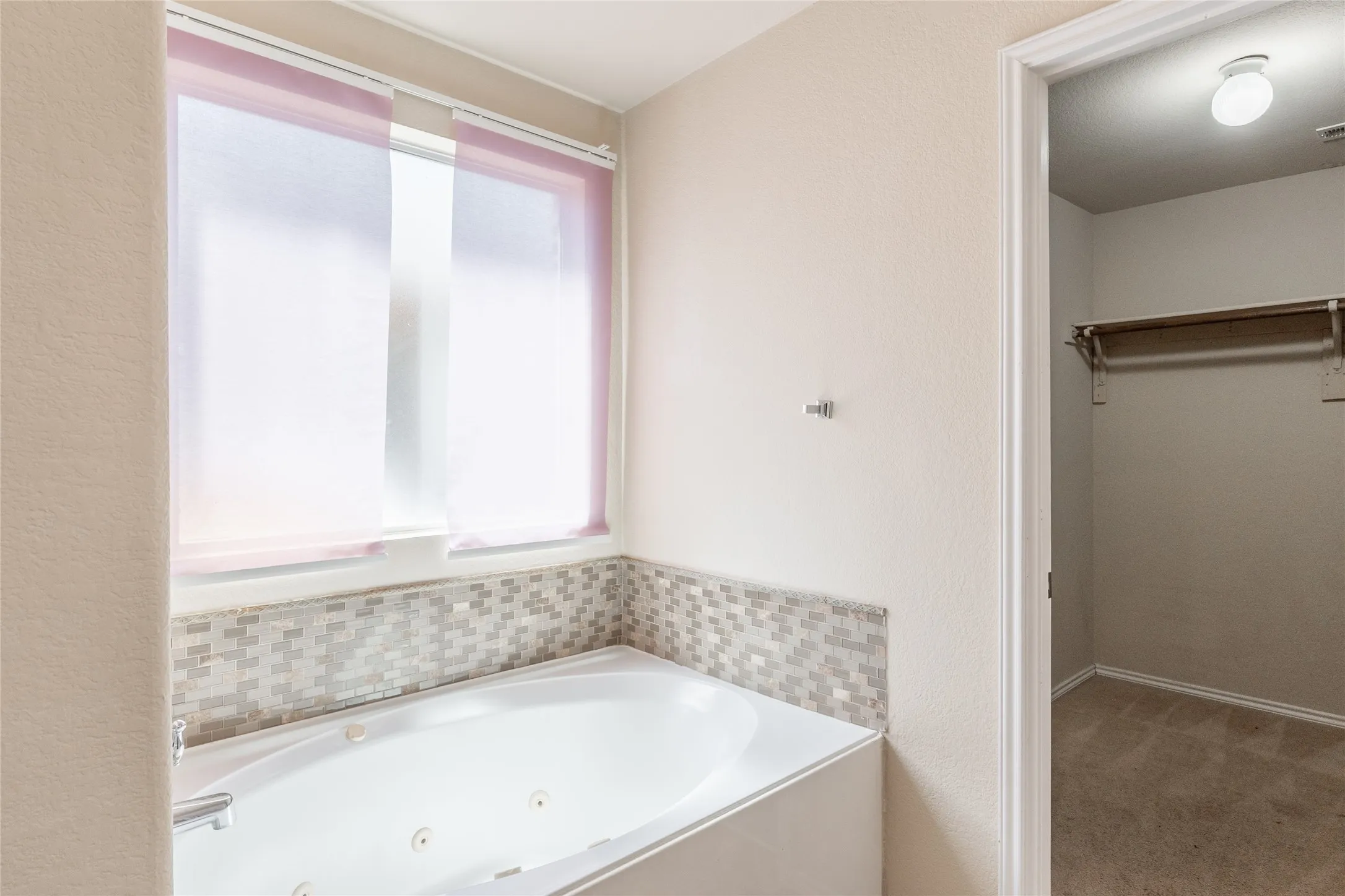 Built-in jetted tub with mosaic tile surround and privacy window treatments