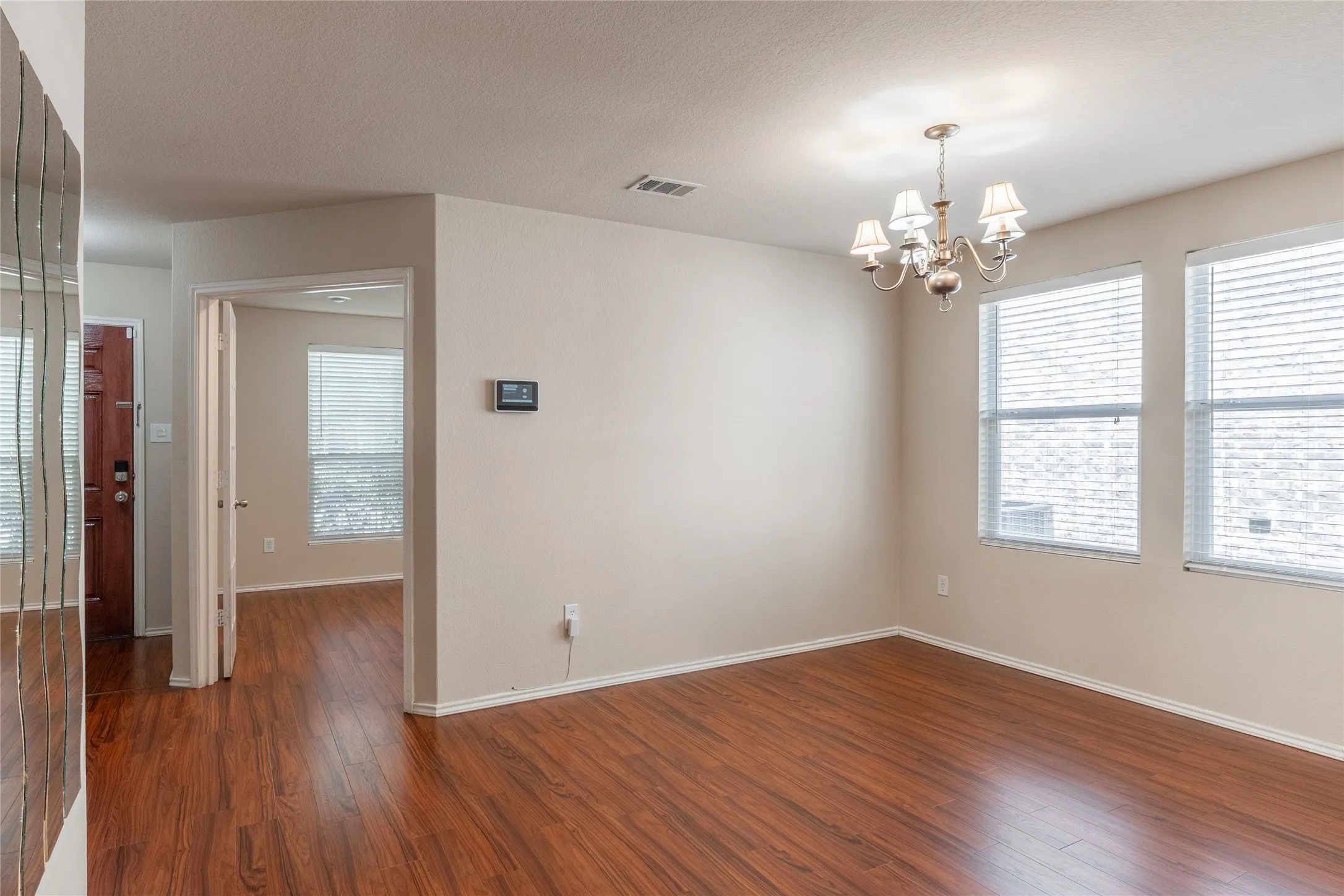 Spacious room featuring wood-finish flooring, light-toned walls, multiple windows with blinds, and an ornate ceiling light fixture