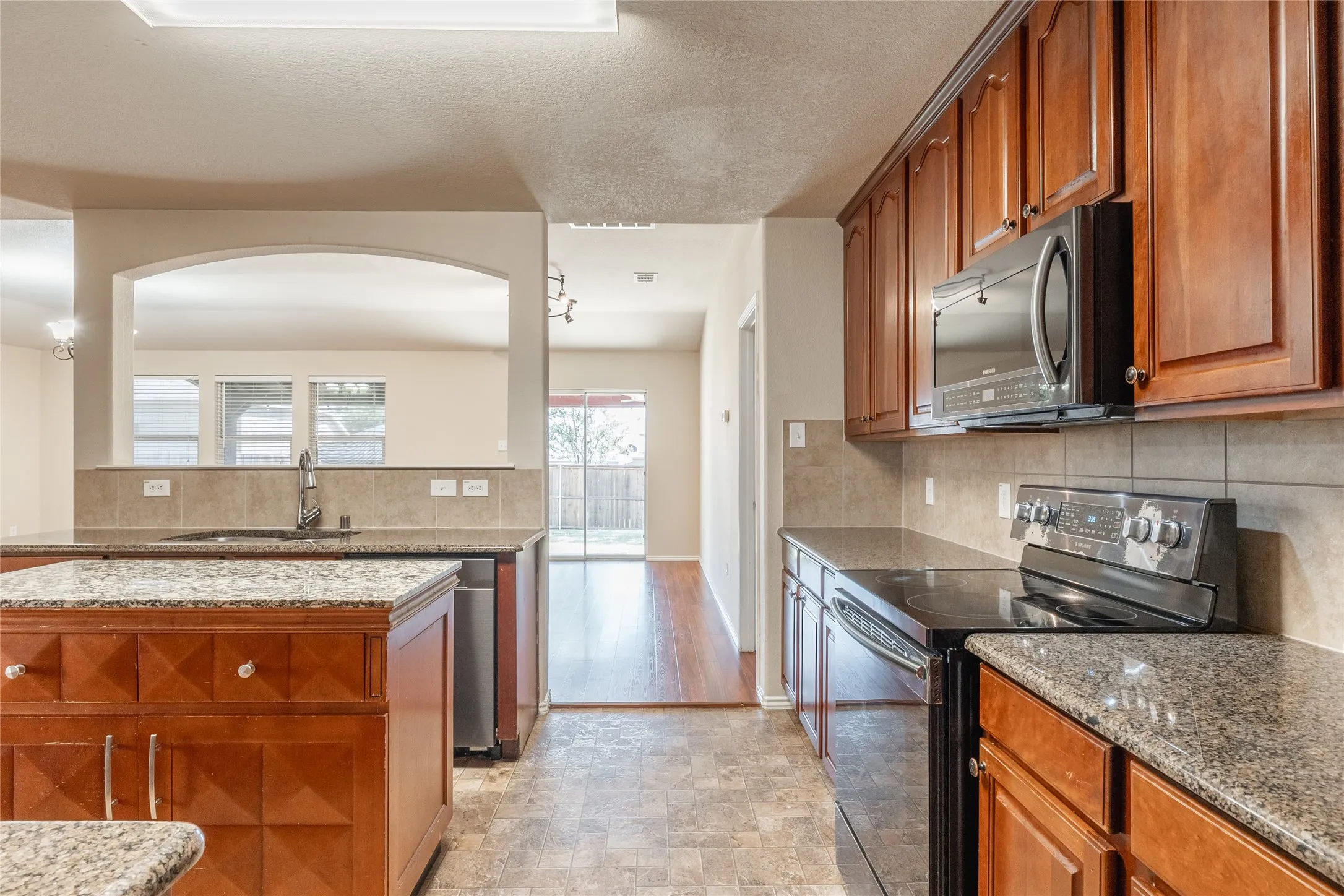 Kitchen featuring wood cabinetry, granite countertops, tile backsplash, and built-in appliances