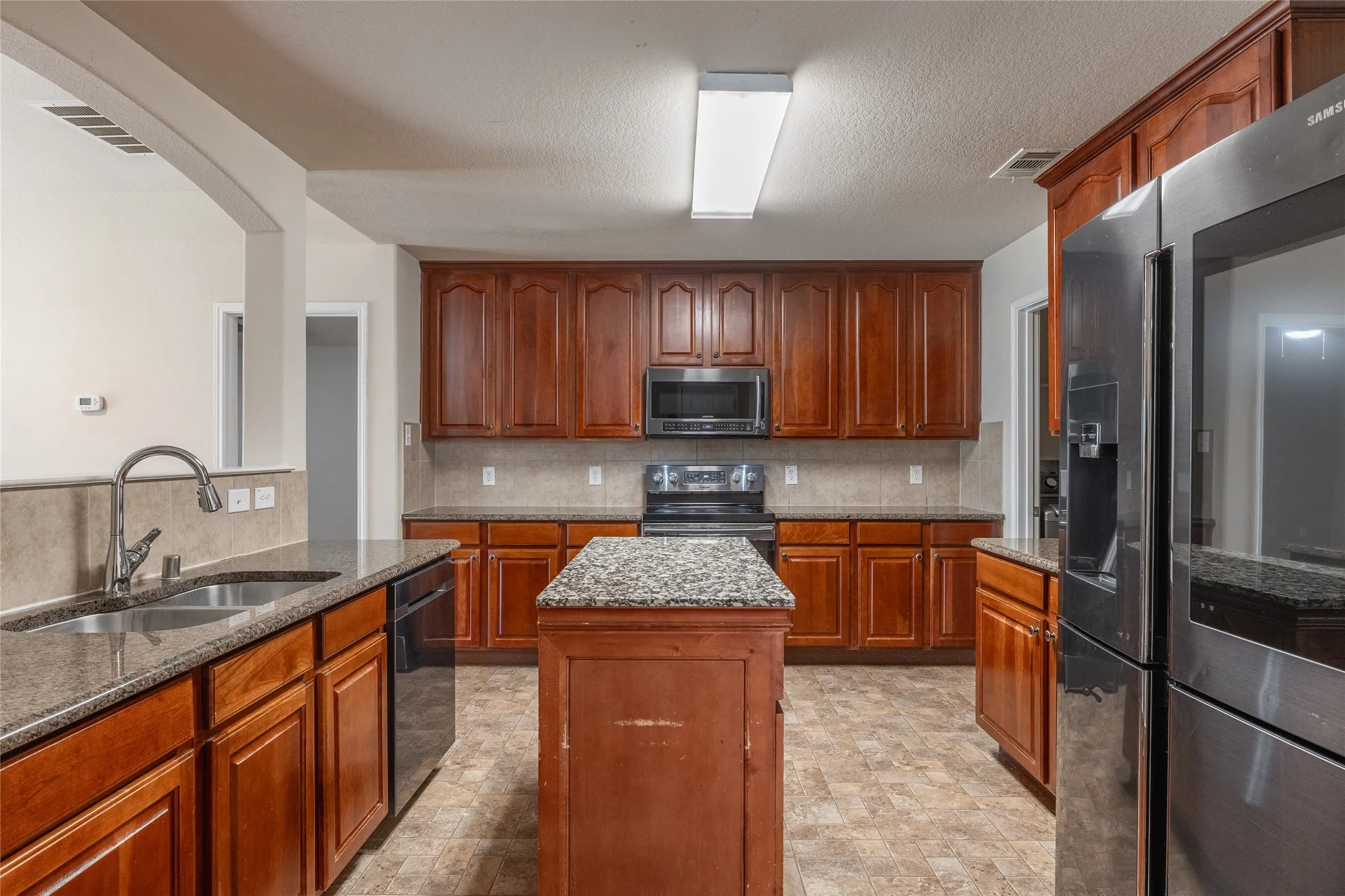 Kitchen featuring wood cabinetry, granite countertops, stainless steel appliances, a center island, and tile flooring