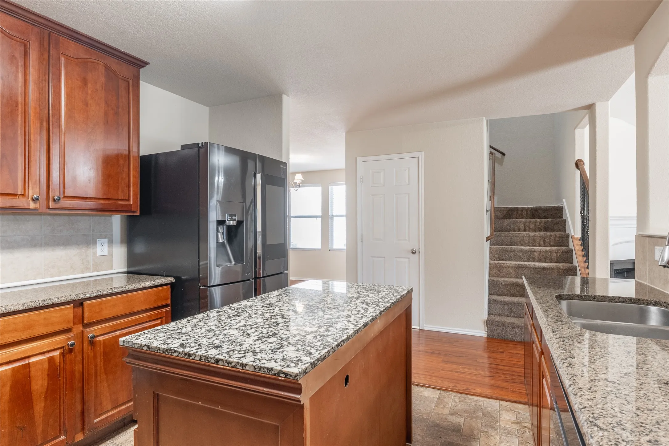 Kitchen featuring a central island with a granite-style countertop, wood cabinetry, tile backsplash, and a stainless steel sink