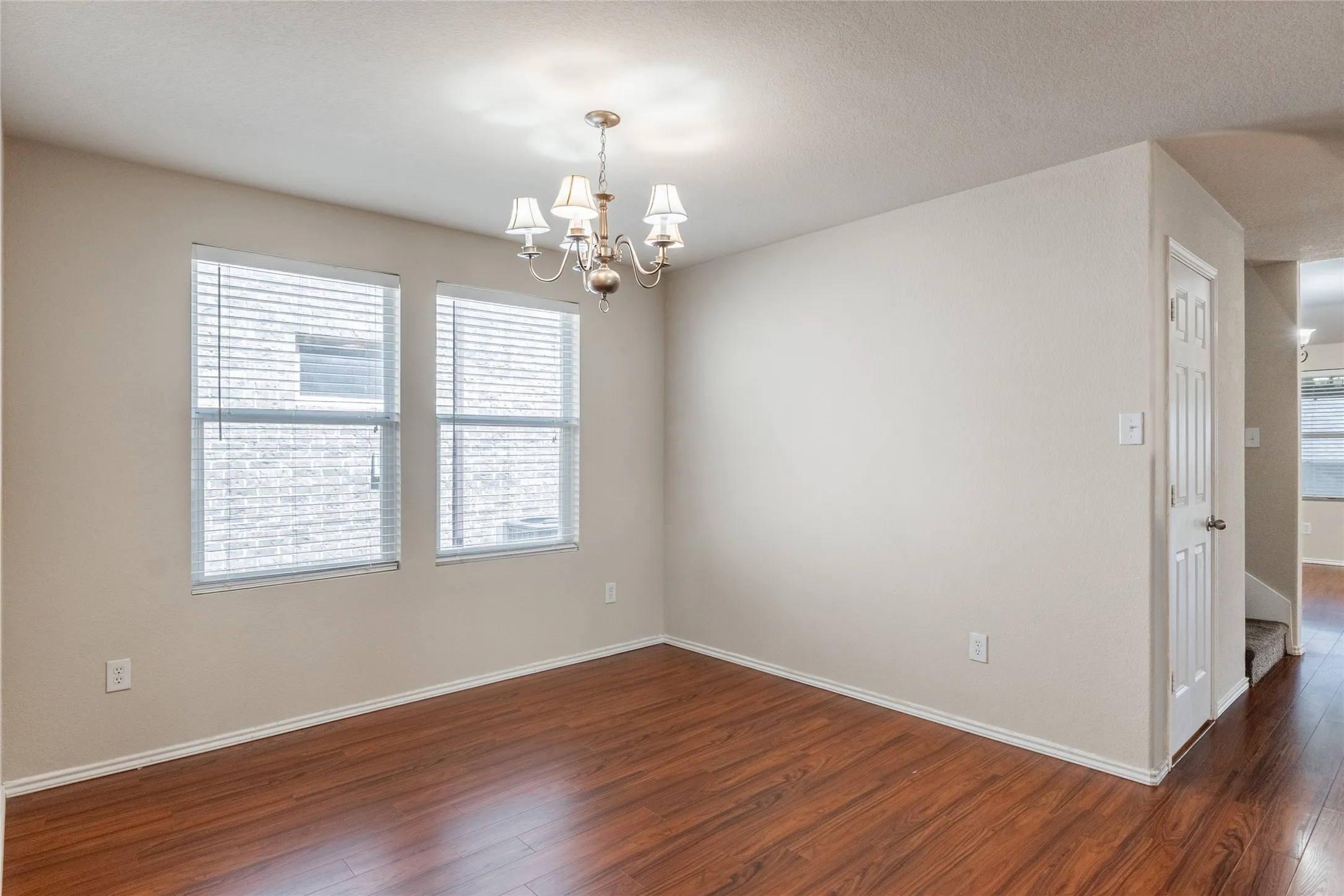 Open room featuring wood-finish flooring, two large windows with blinds, and a decorative chandelier