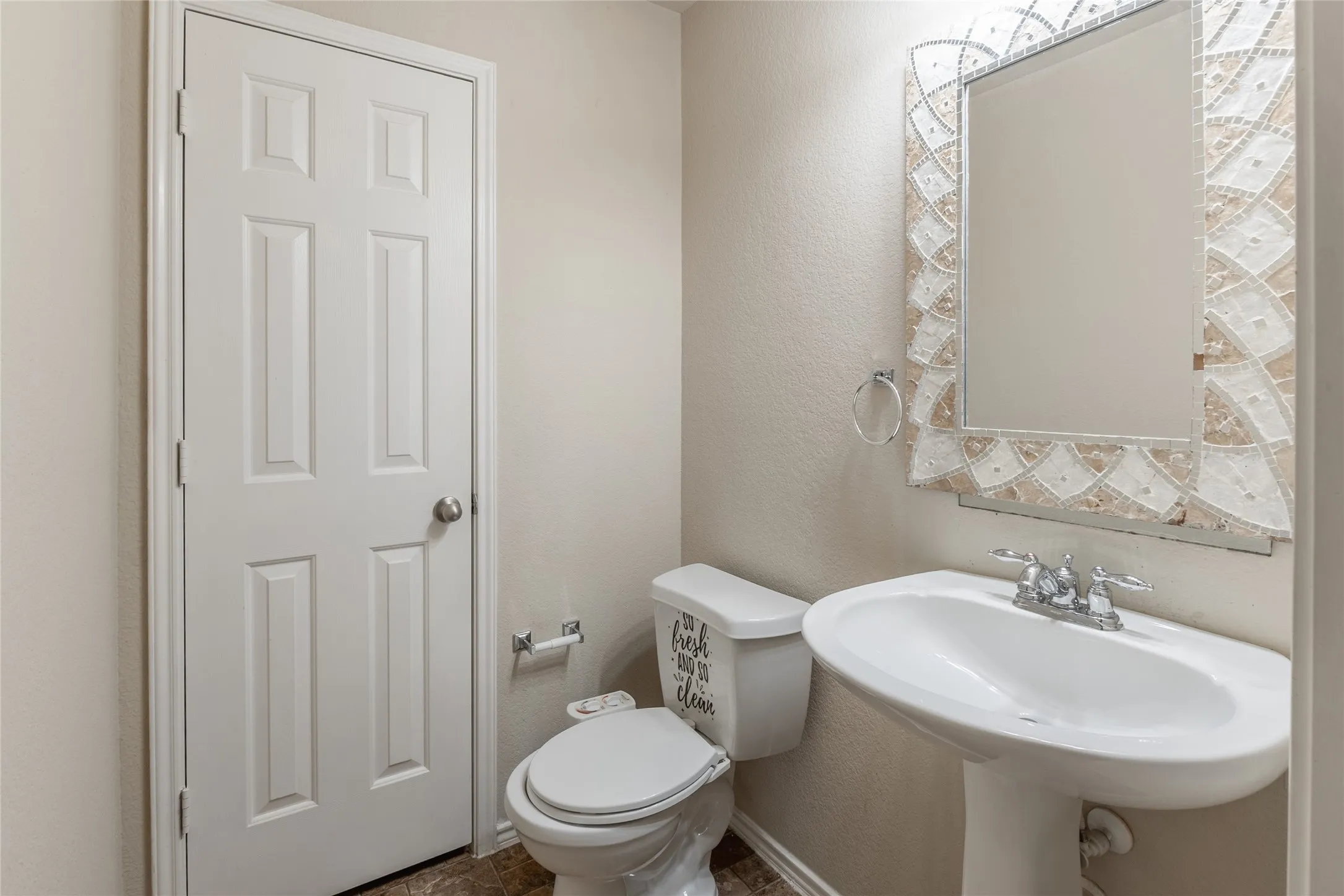 Pedestal sink with chrome faucet, decorative tile-framed mirror, and paneled interior door