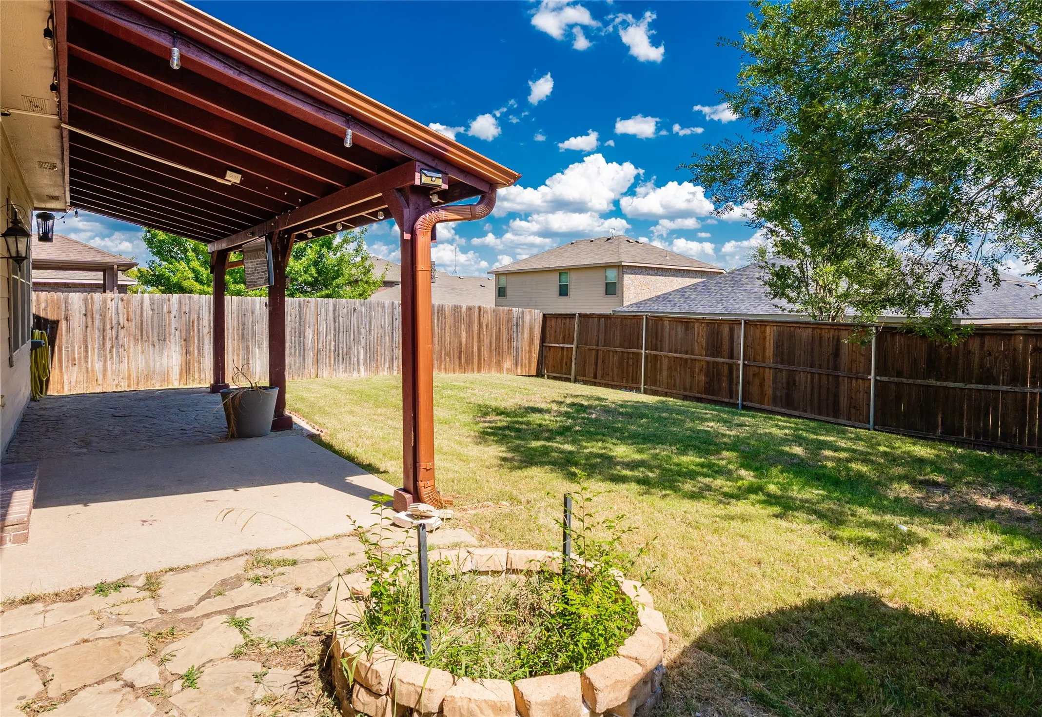 Spacious backyard featuring a covered patio, expansive lawn, stone-edged planting bed, and privacy fencing