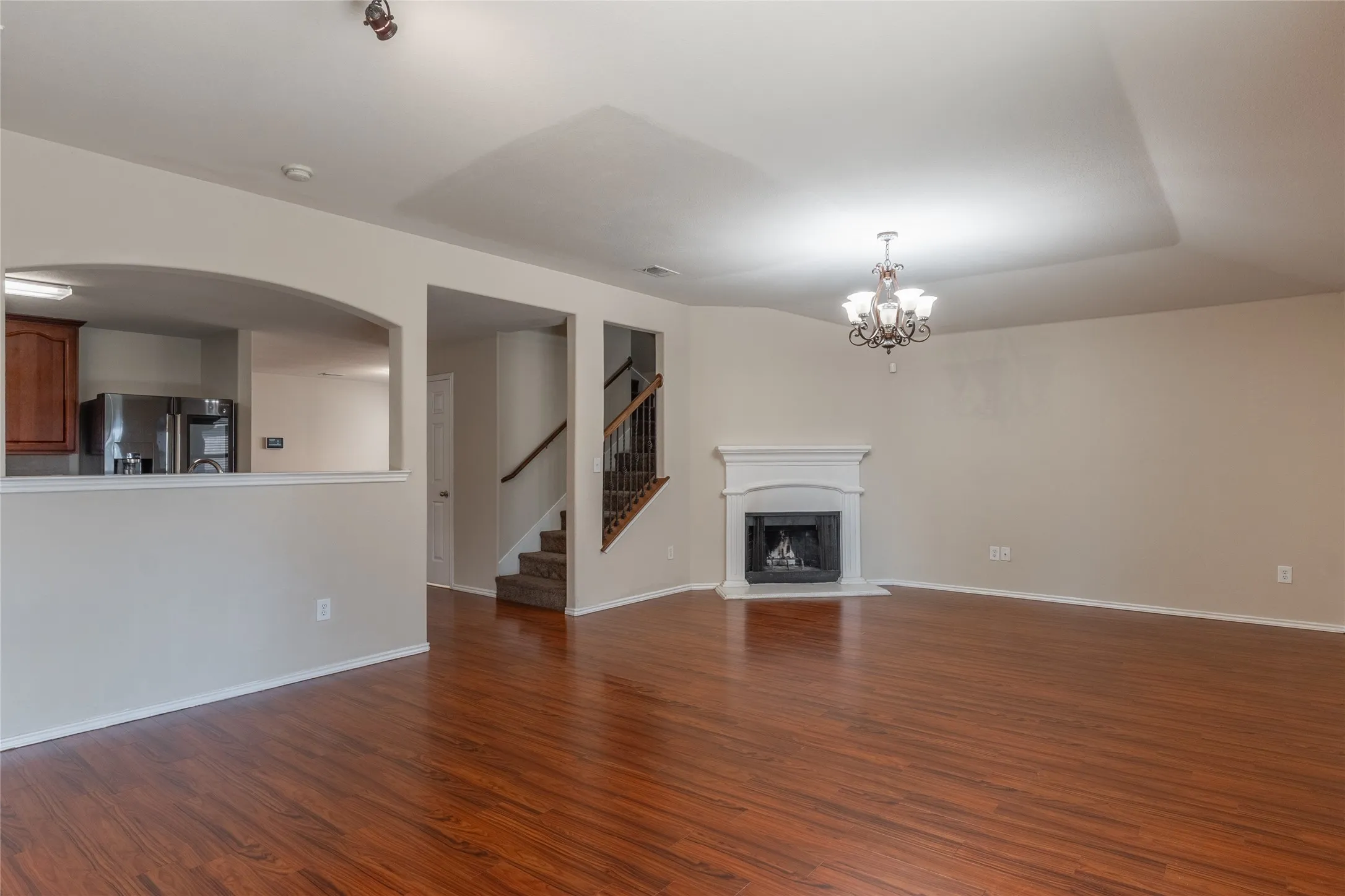 Spacious living area featuring wood-finish flooring, a white mantel fireplace, tray ceiling, and a decorative chandelier