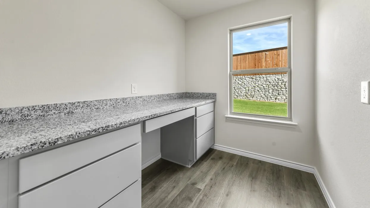 Built-in desk cabinetry with a light speckled countertop, wood-finish flooring, and a window providing natural illumination
