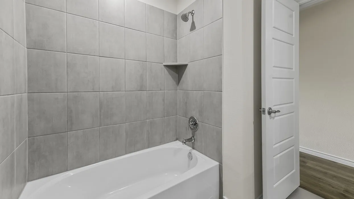 Bathtub with light gray subway tile surround and integrated corner shelf