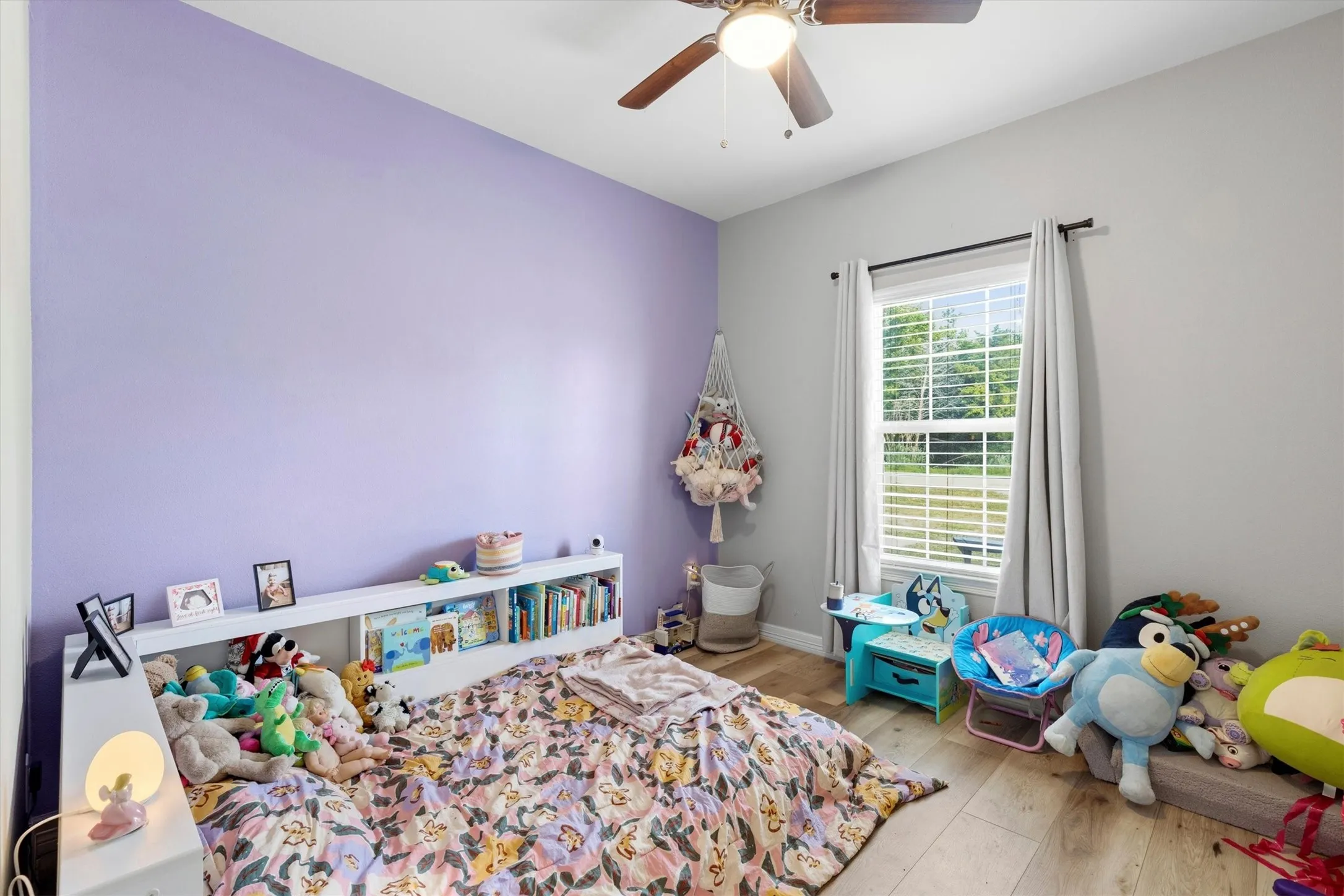 Room featuring a ceiling fan with light fixture, window with blinds and drapes, and wood-finish flooring
