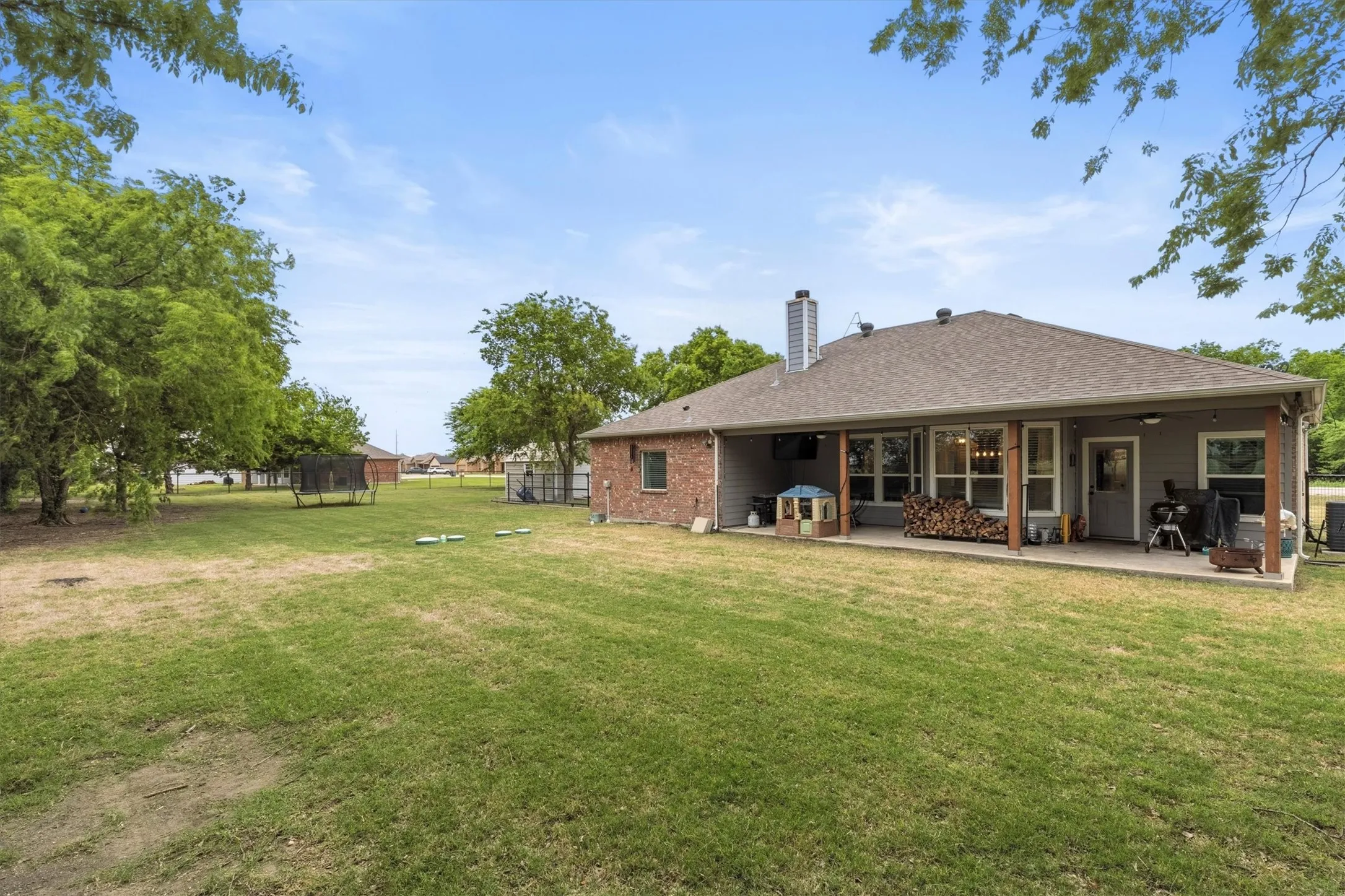 Expansive backyard featuring a manicured lawn, mature trees, and a covered patio area