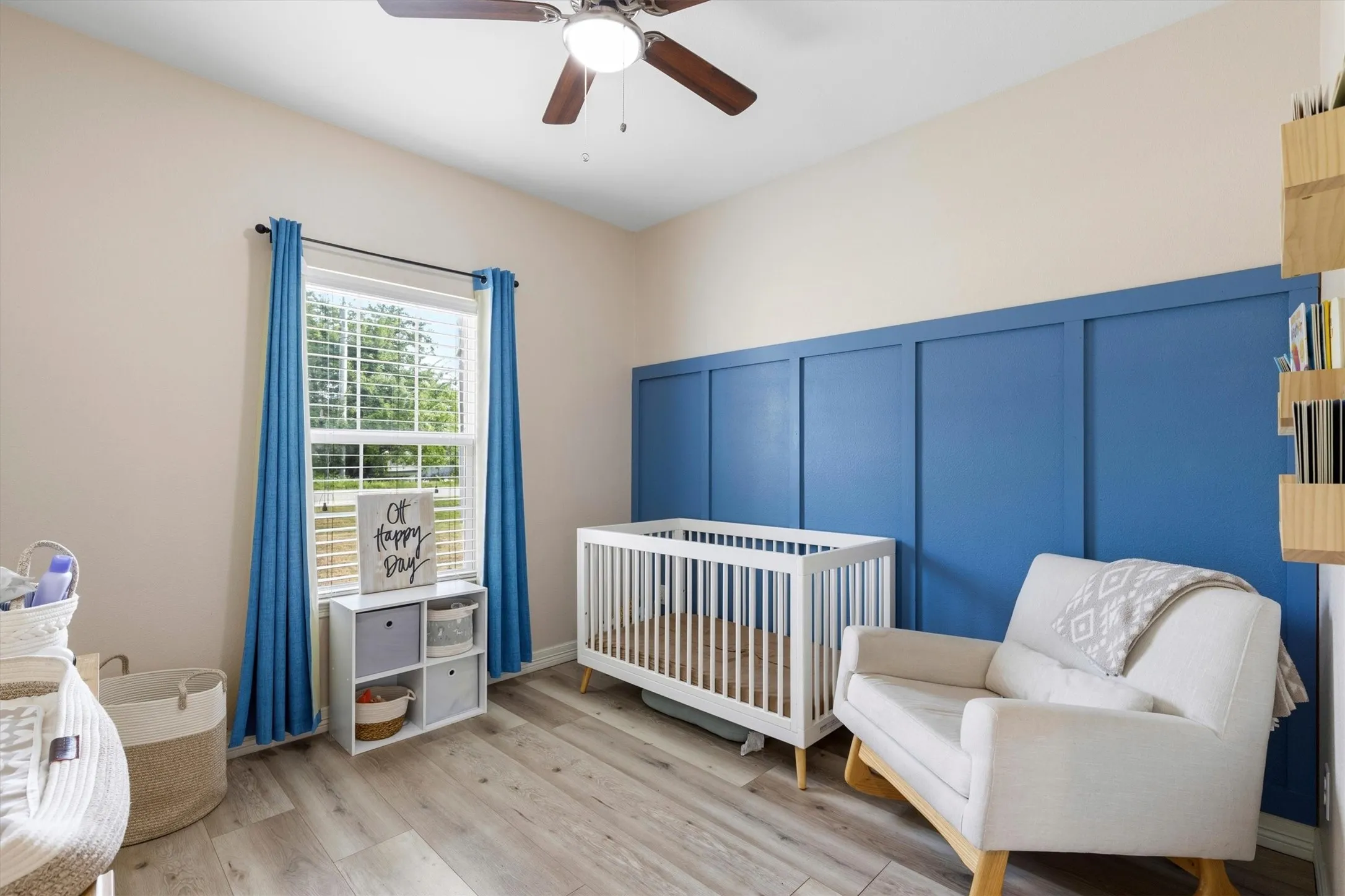 Room featuring wood-finish flooring, a contemporary ceiling fan, and a prominent accent wall with blue board and batten detailing