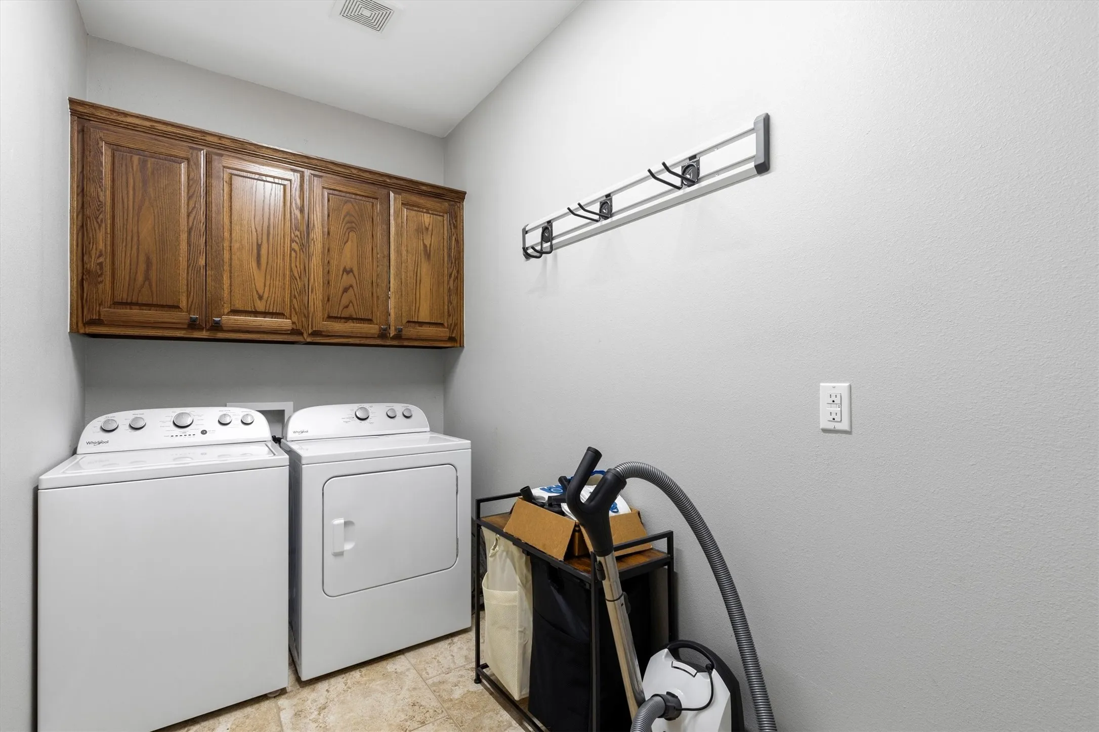 Laundry area featuring wood-finish cabinetry, neutral wall paint, and tiled flooring