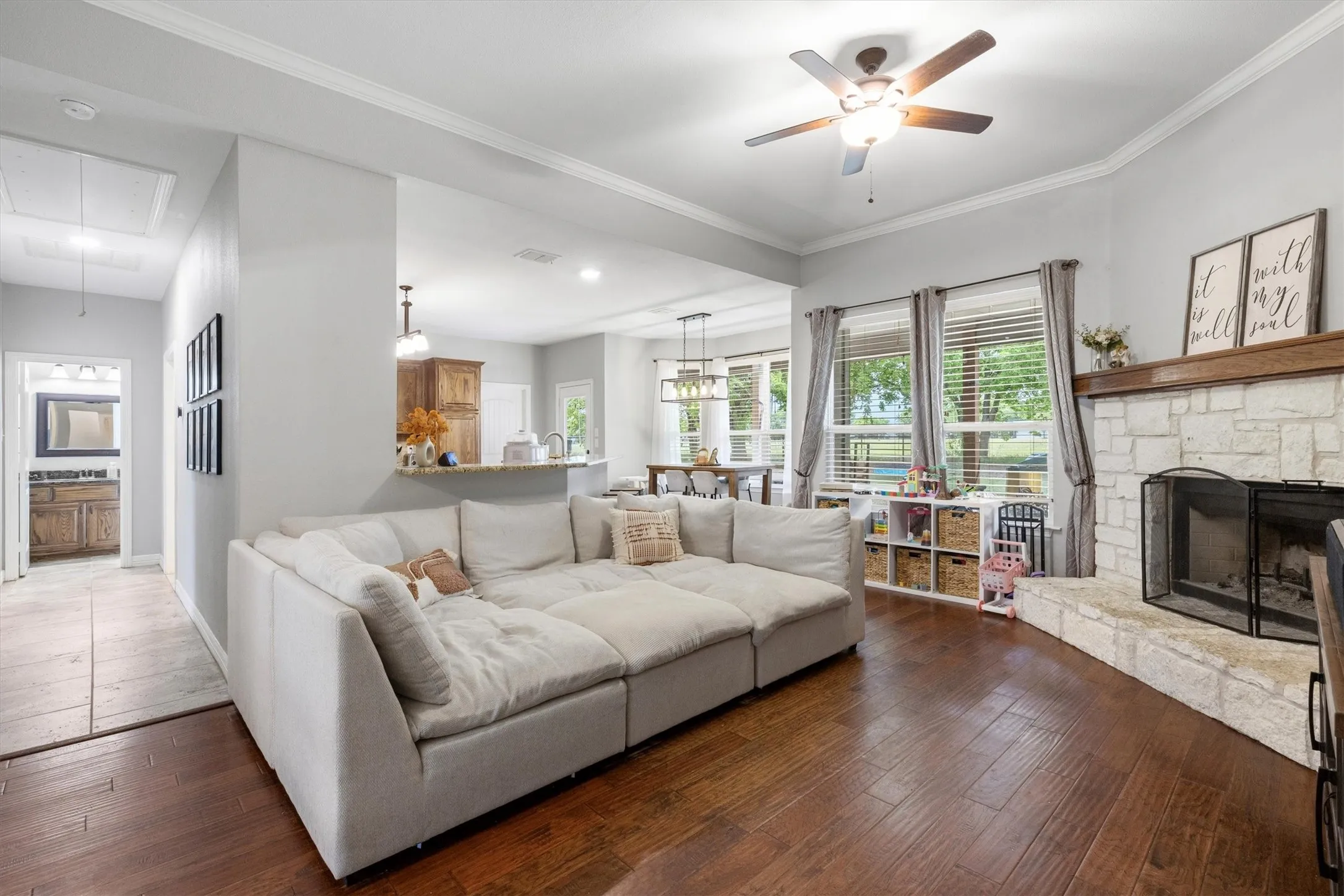 Living area featuring wood-finish flooring, a stone fireplace with a wood mantel, and crown molding