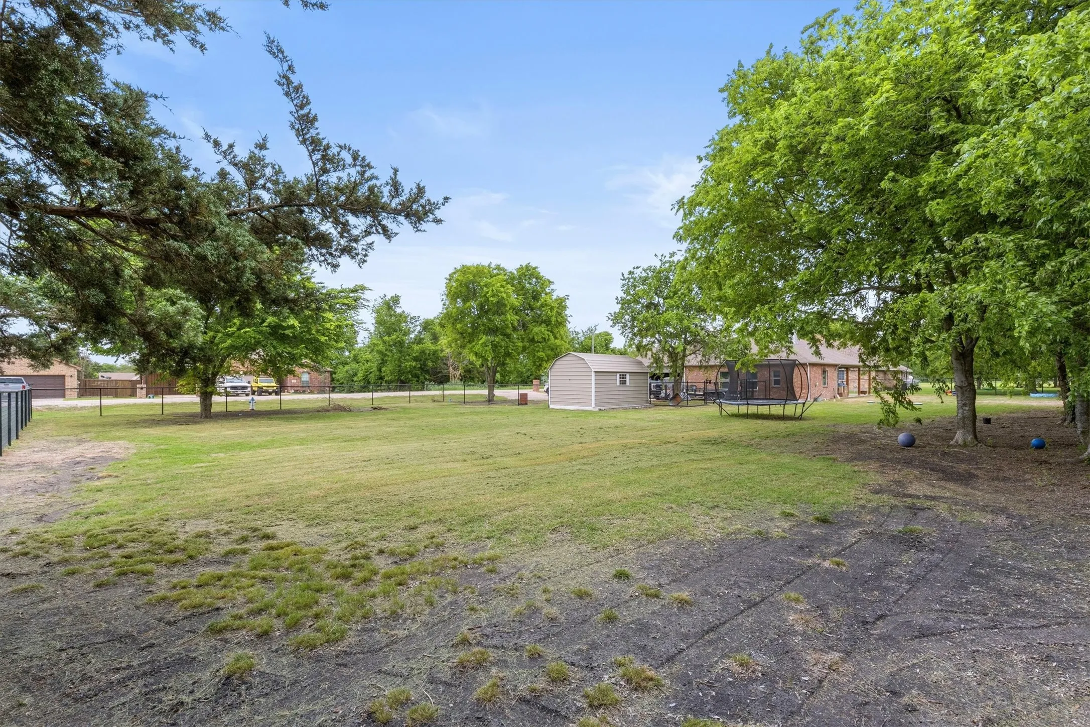 Expansive green space featuring established trees, a fenced perimeter, and a detached storage shed
