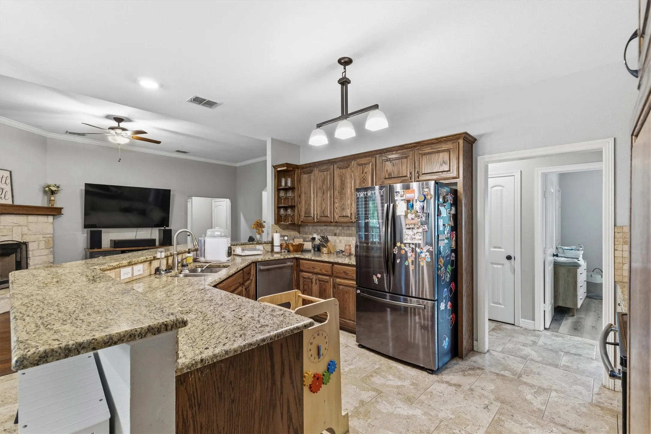 Expansive kitchen featuring light-toned tile flooring, granite countertops, wood cabinetry, and stainless steel appliances