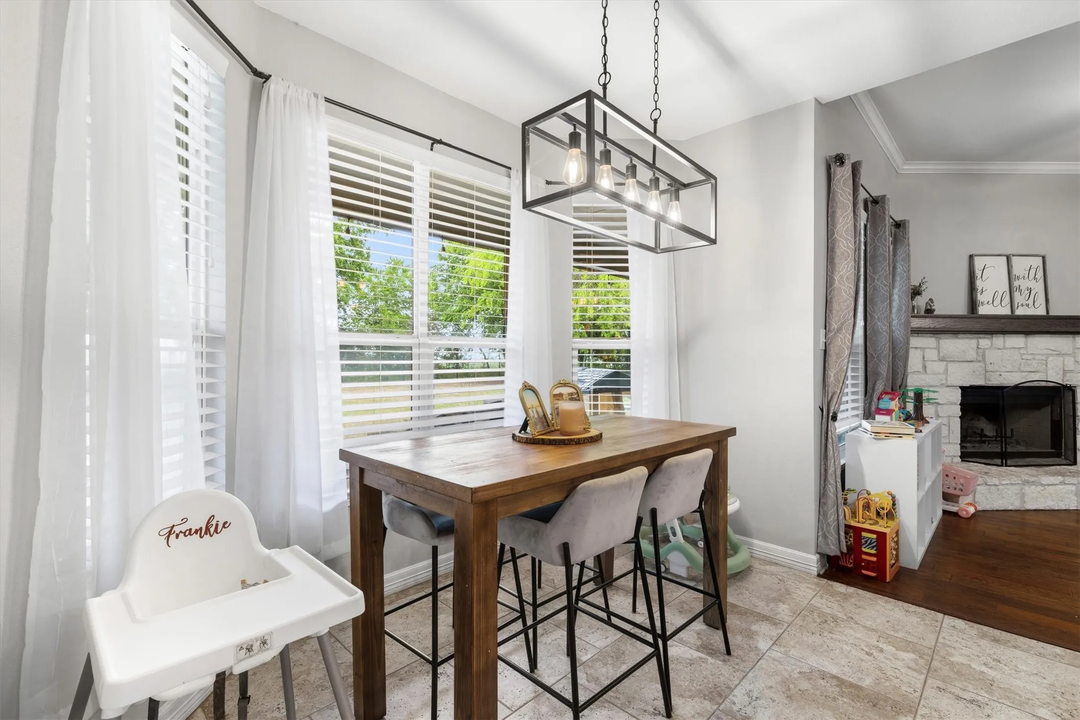 Open-concept dining area featuring multiple windows, a stone fireplace, light-toned walls, and tile flooring