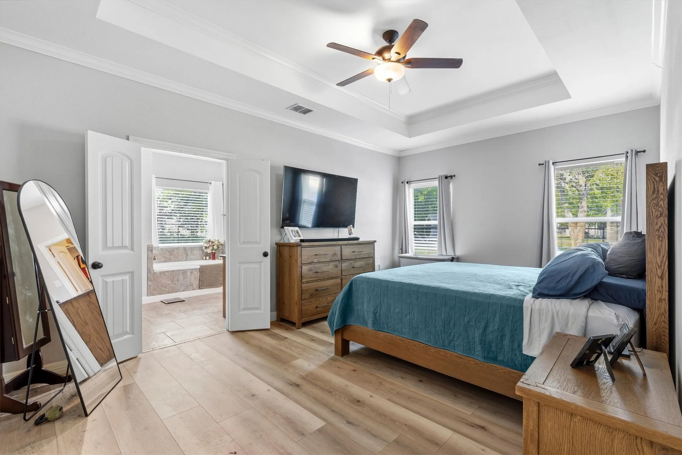 Bedroom featuring wood-finish flooring, a tray ceiling with a ceiling fan, and two windows