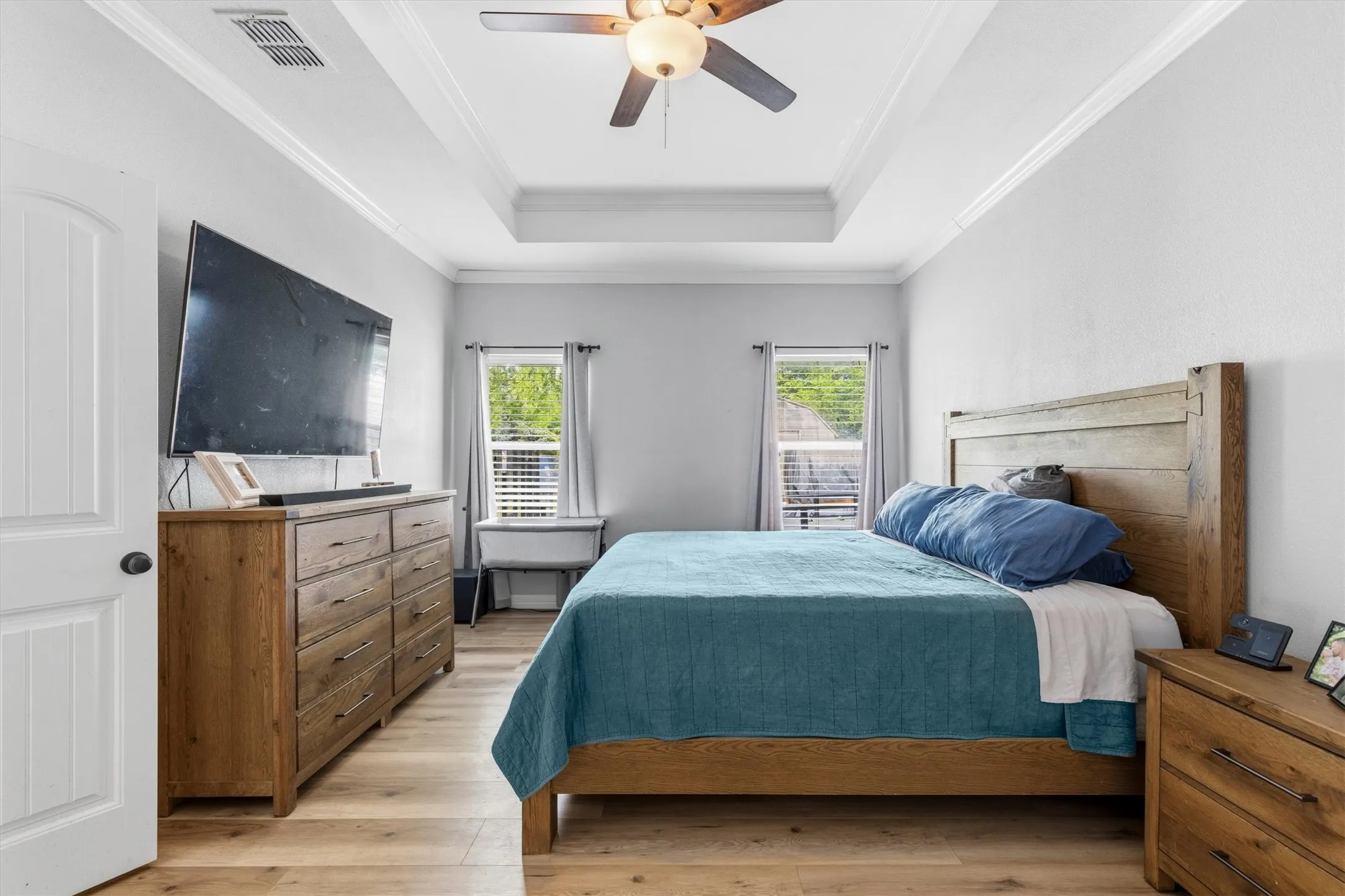 Spacious bedroom featuring wood-finish flooring, a tray ceiling with crown molding, and a ceiling fan
