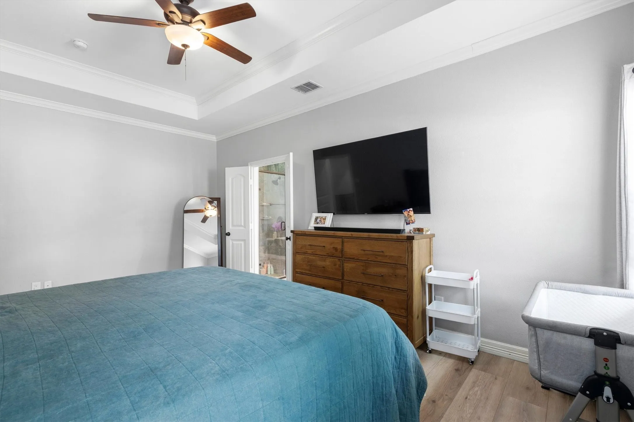 Recessed tray ceiling with crown molding, wood-finish flooring, and a ceiling fan with integrated lighting