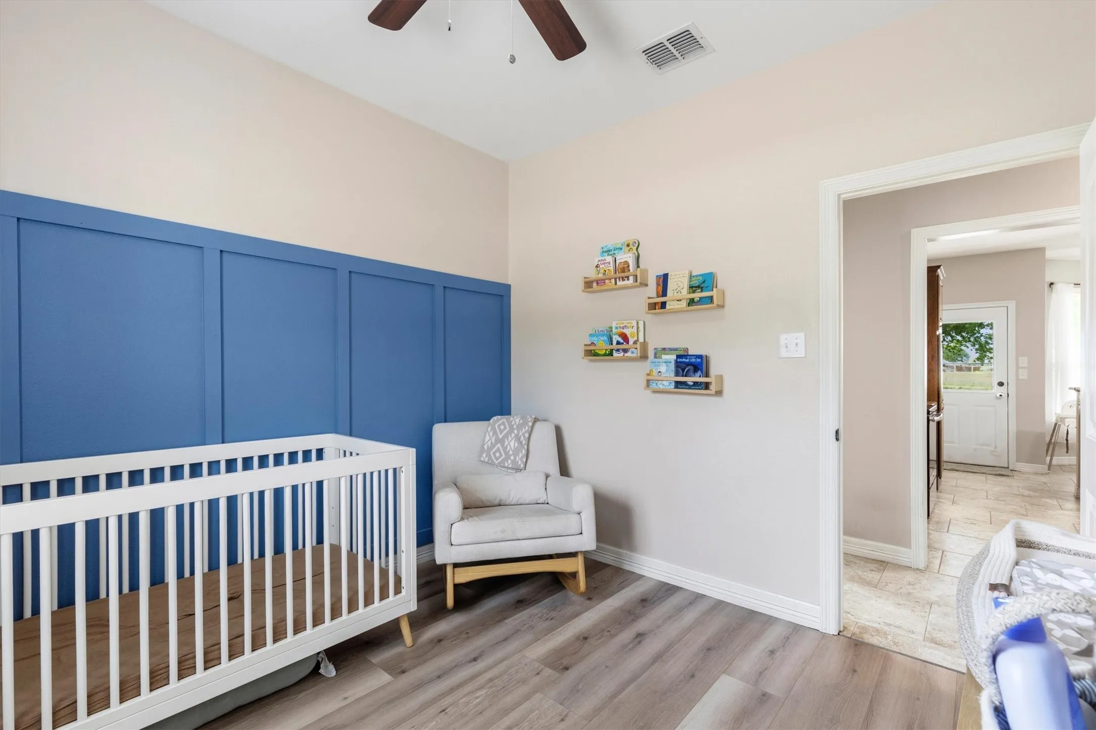 Room featuring wood-finish flooring, a decorative blue board and batten accent wall, and a ceiling fan