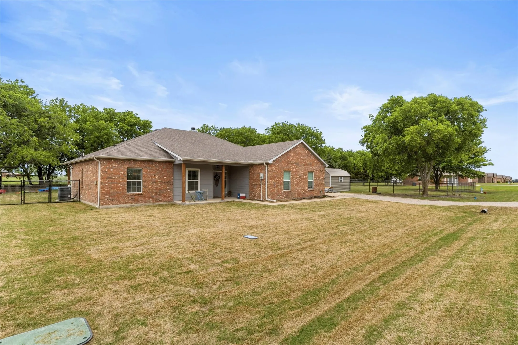 Brick and siding exterior featuring a covered porch, fenced side yard, an outbuilding, and a gravel driveway