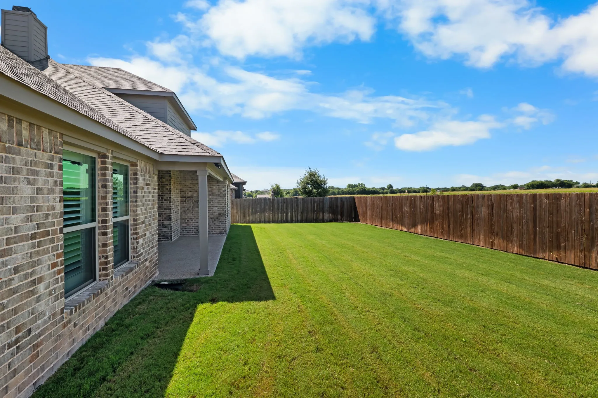Spacious backyard featuring a manicured lawn, full privacy fence, and a covered patio area