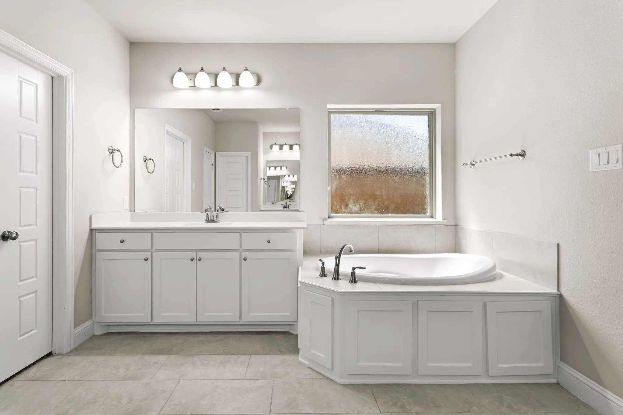 Bright bathroom featuring a built-in garden tub, a single vanity with storage cabinetry, a large wall-mounted mirror, and tile flooring