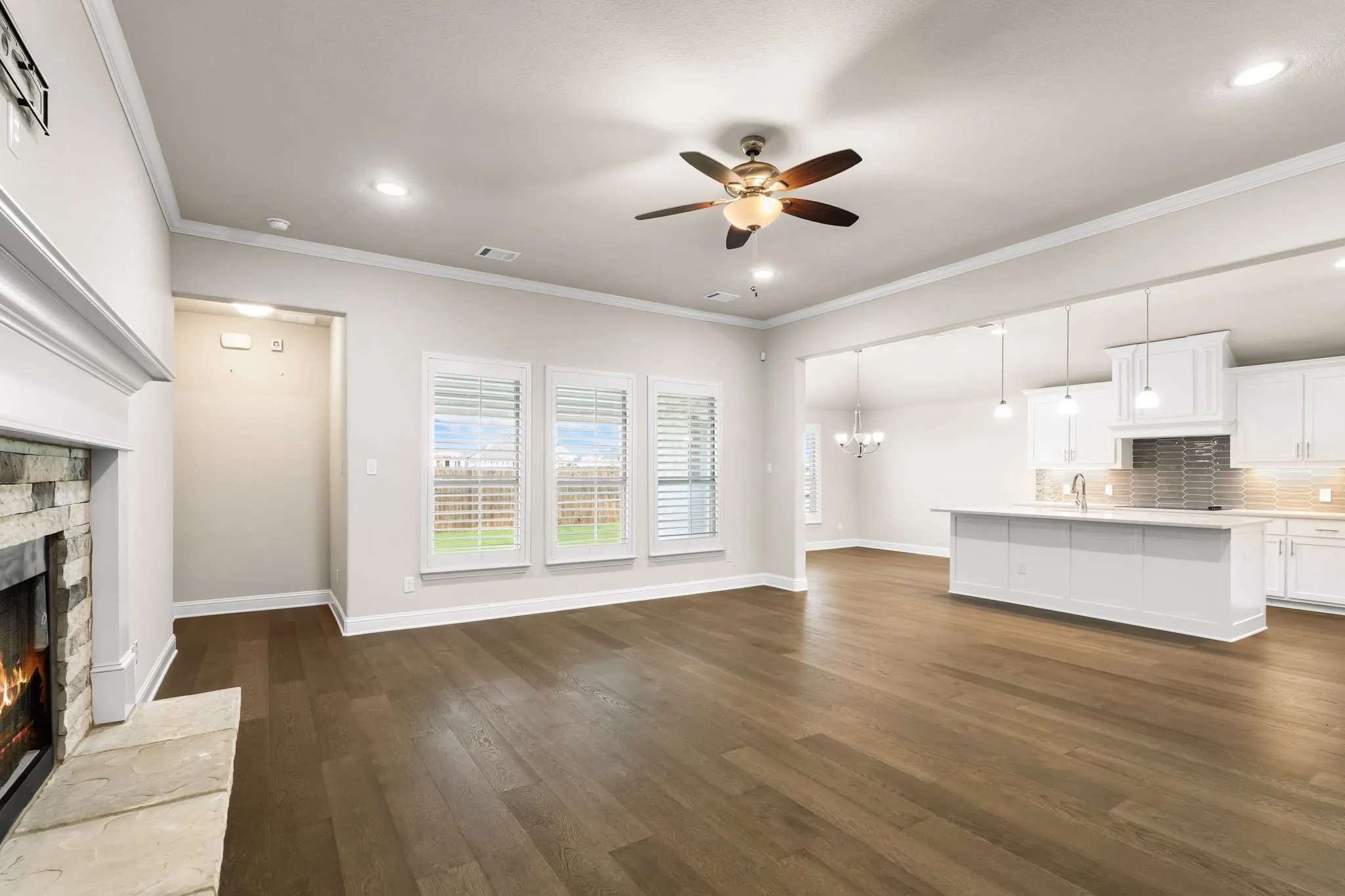 Open-concept living space featuring wood-finish flooring, a stone-faced fireplace with hearth, recessed lighting, and a ceiling fan