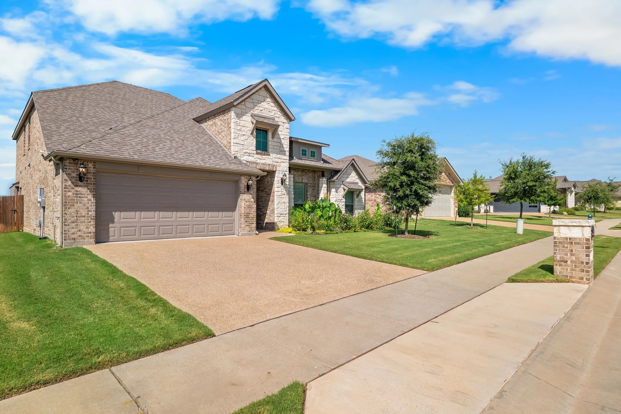 Stone and brick exterior featuring a two-car garage, concrete driveway, and established front landscaping