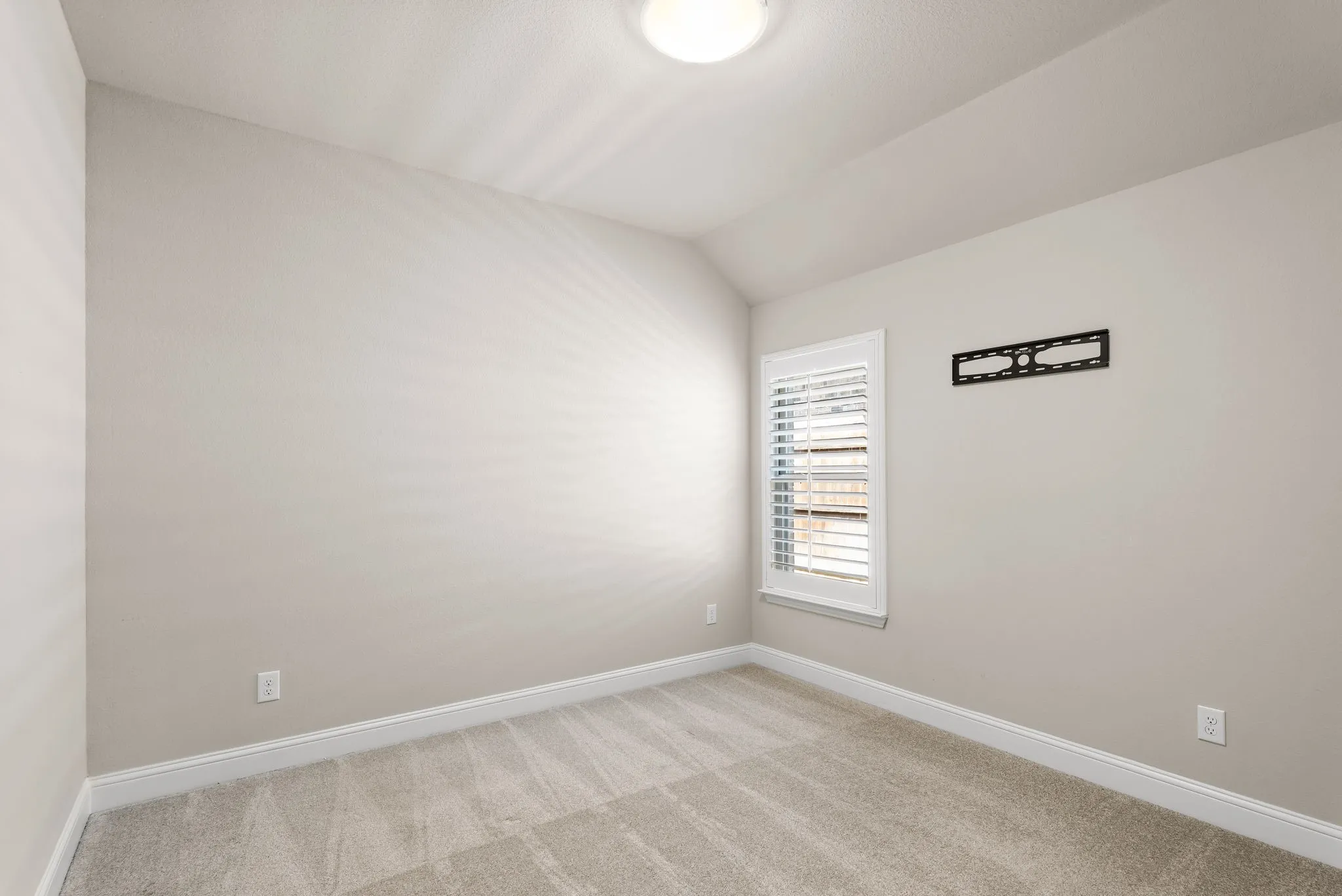 Neutral-toned room featuring a single window with white plantation shutters, light gray wall paint, and complementing carpet flooring