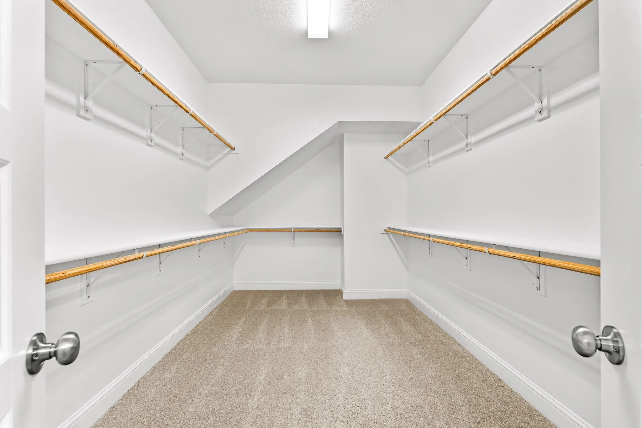 Walk-in closet featuring light beige carpet flooring, white walls, and multiple levels of wooden hanging rods with shelving